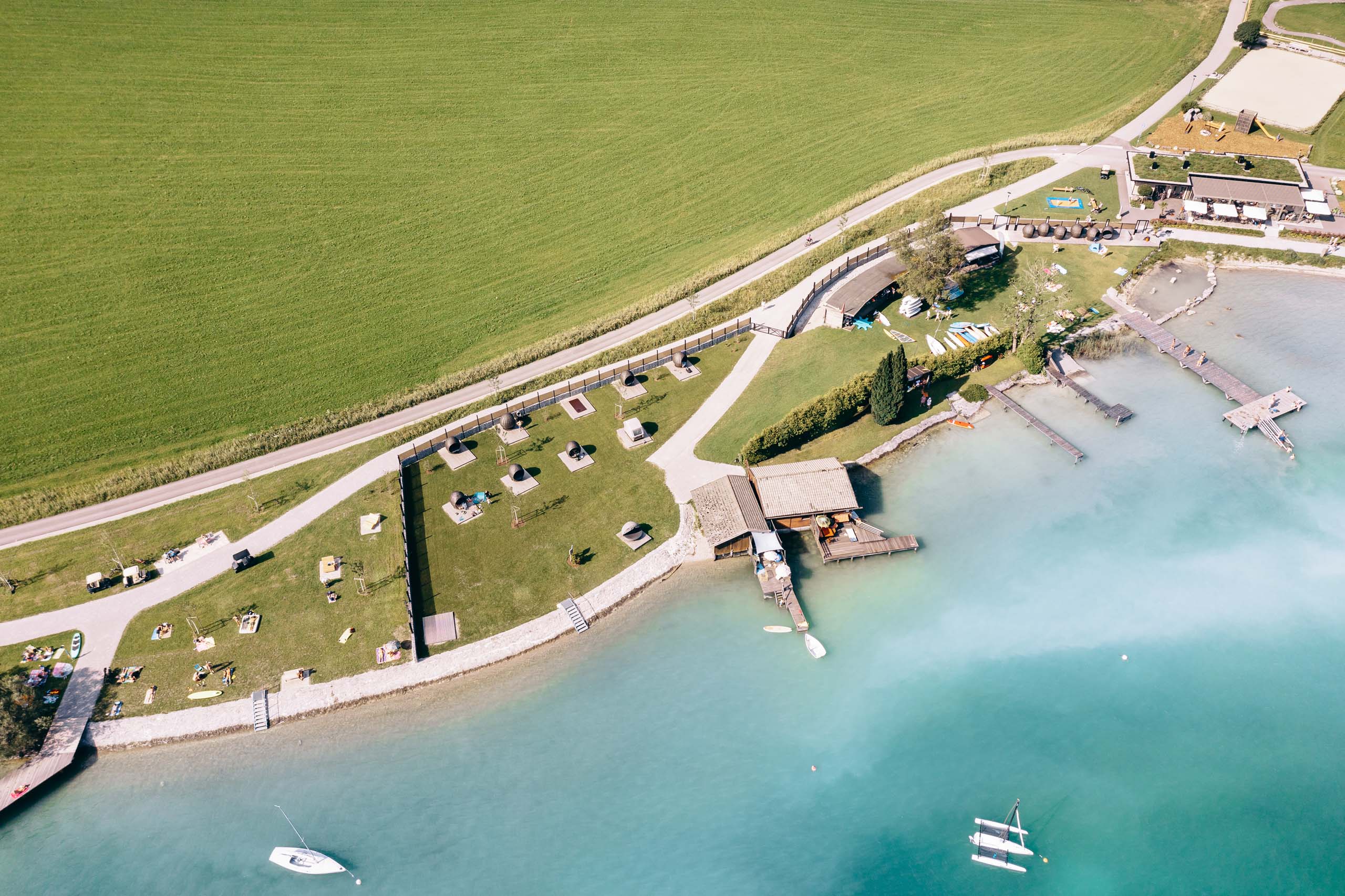 Familiennestl Seeblick II Luftaufnahme Strandabschnitt mit Kanonen, Booten und grüner Wiese am Seeufer