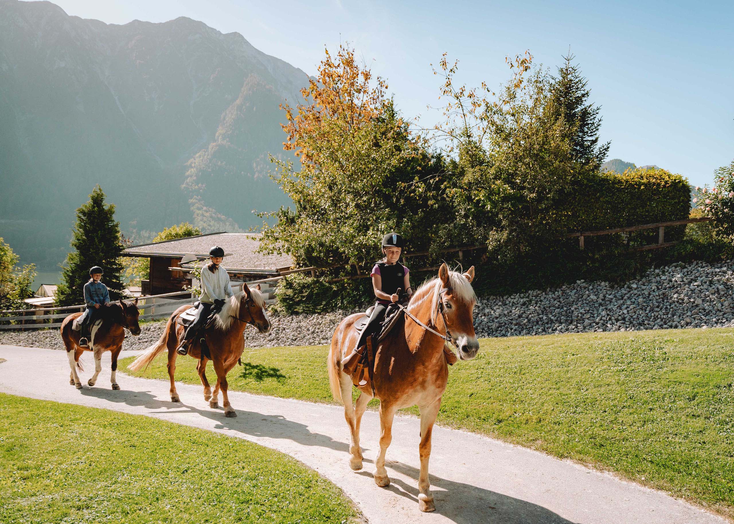Familiennestl Seeblick II Drei Kinder reiten auf Pferden auf einem Weg vor einer Berglandschaft