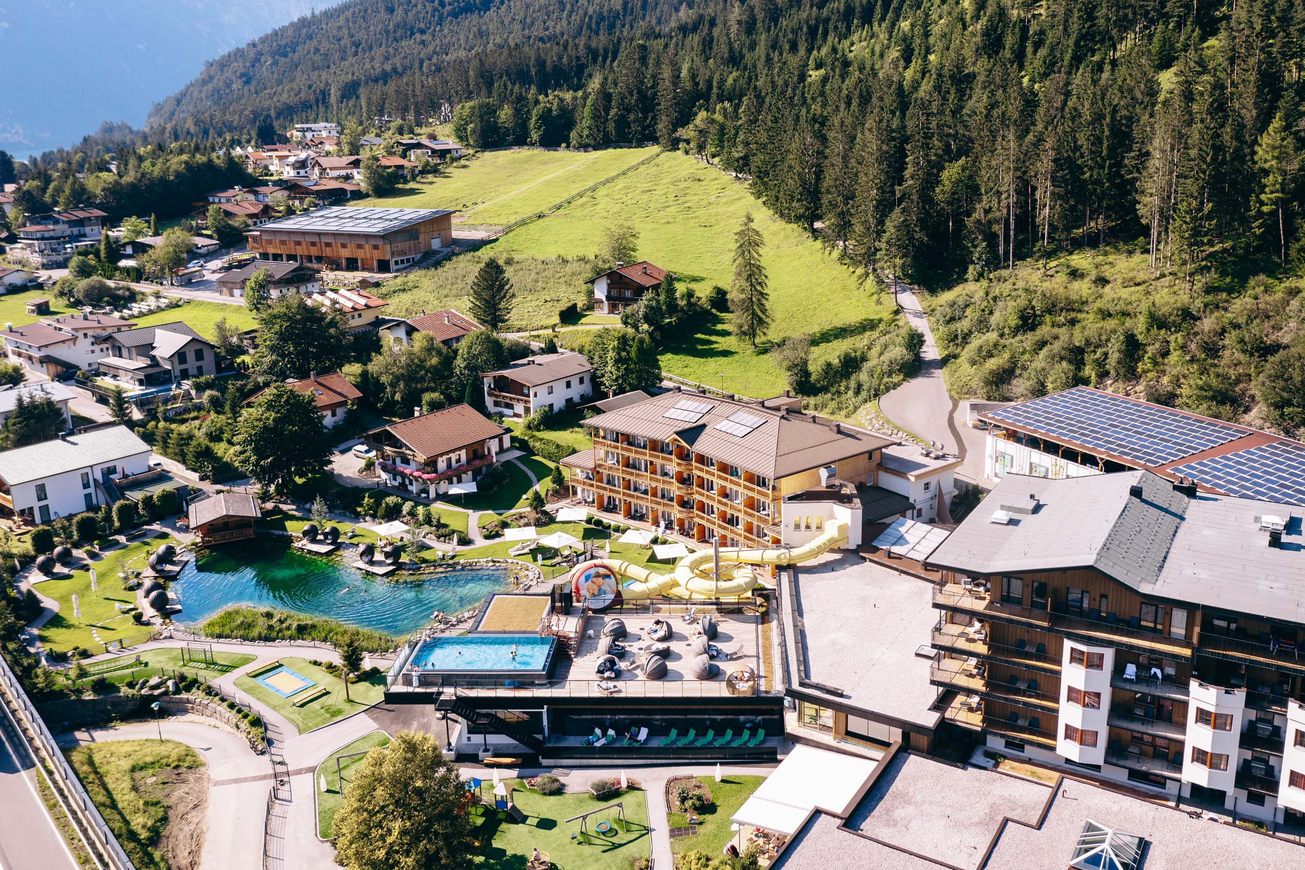Familiennestl Seeblick II Luftaufnahme eines Resorts mit Swimmingpools und Wasserrutsche in grüner Alpenlandschaft