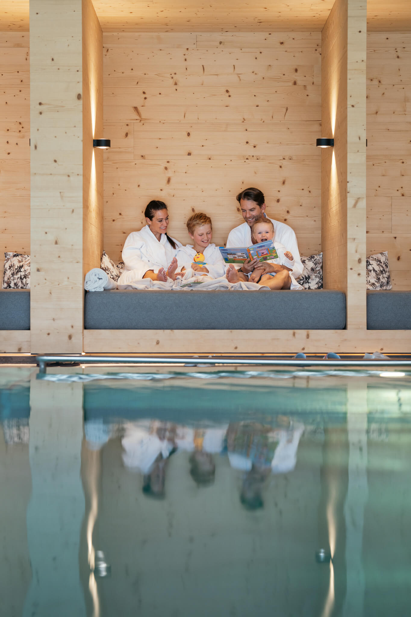 Familiennestl Seeblick II Familie in Bademänteln sitzt gemütlich an einem Holzruheraum neben dem Pool