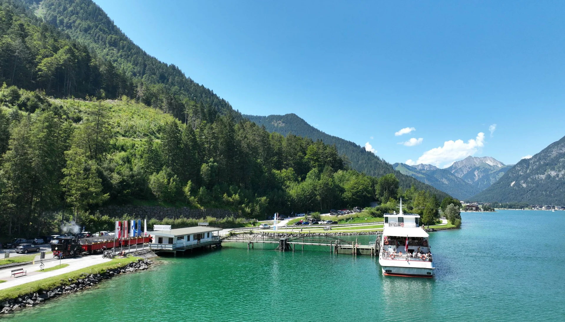 Ihr abenteuerlicher Erlebnisurlaub in Österreich Grünes Bergseeufer mit Dampflock und Ausflugsboot bei Sonnenschein