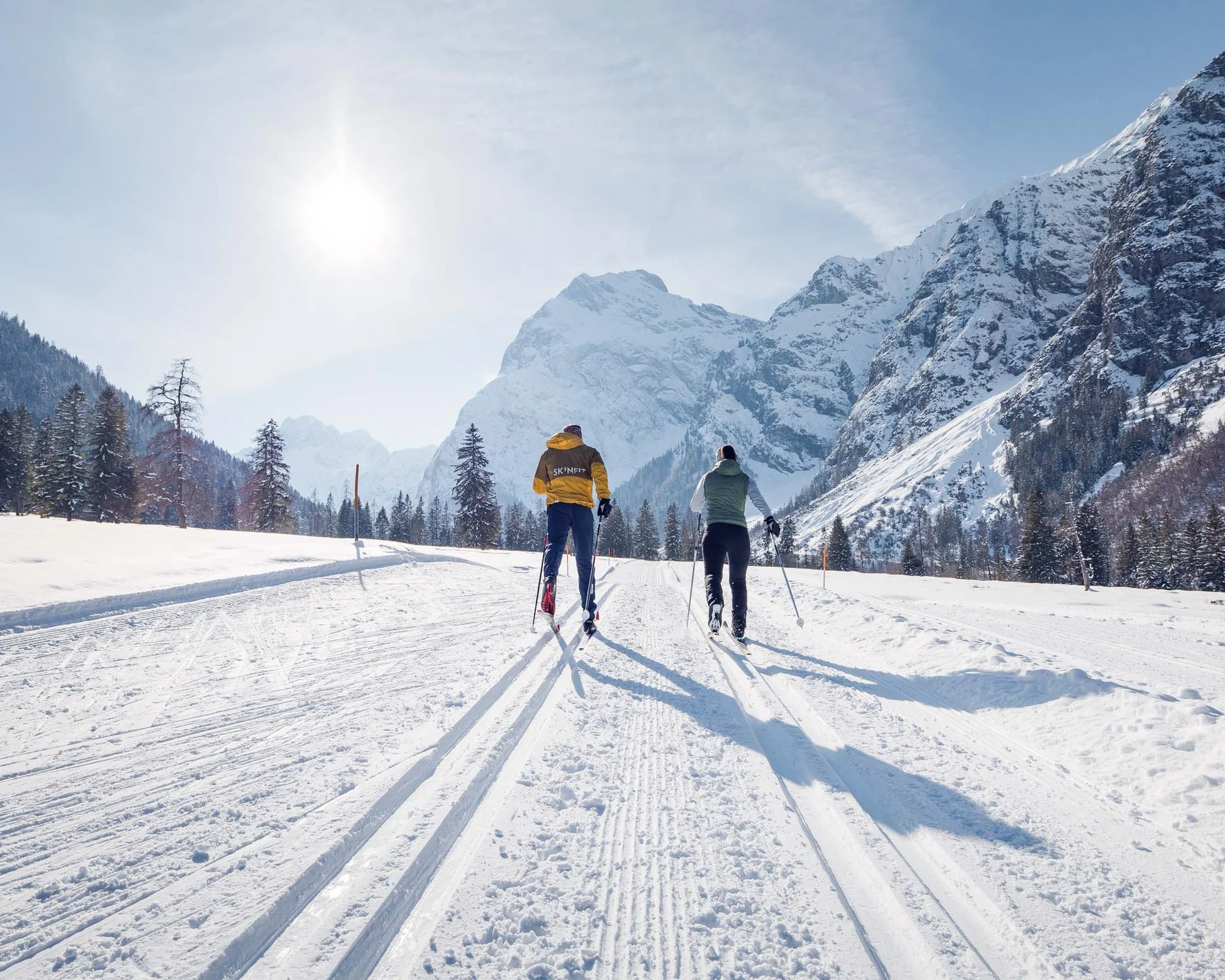 Ihr abenteuerlicher Erlebnisurlaub in Österreich Zwei Menschen beim Langlaufen auf verschneiter Bergstrecke unter Sonnenschein