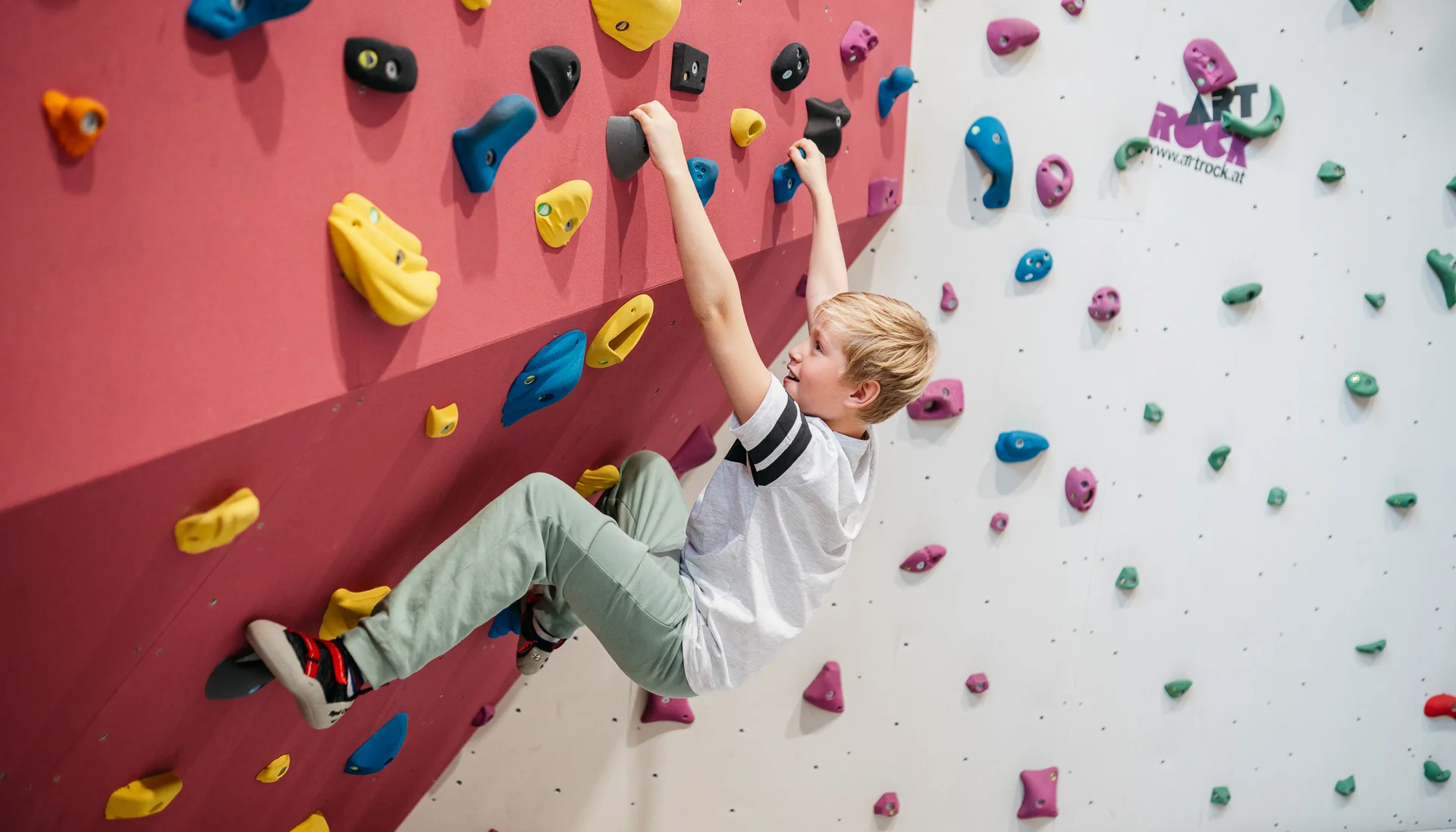 Action im Hotel mit Kletterhalle Junge klettert an bunten Griffen an einer Kletterwand in der Halle