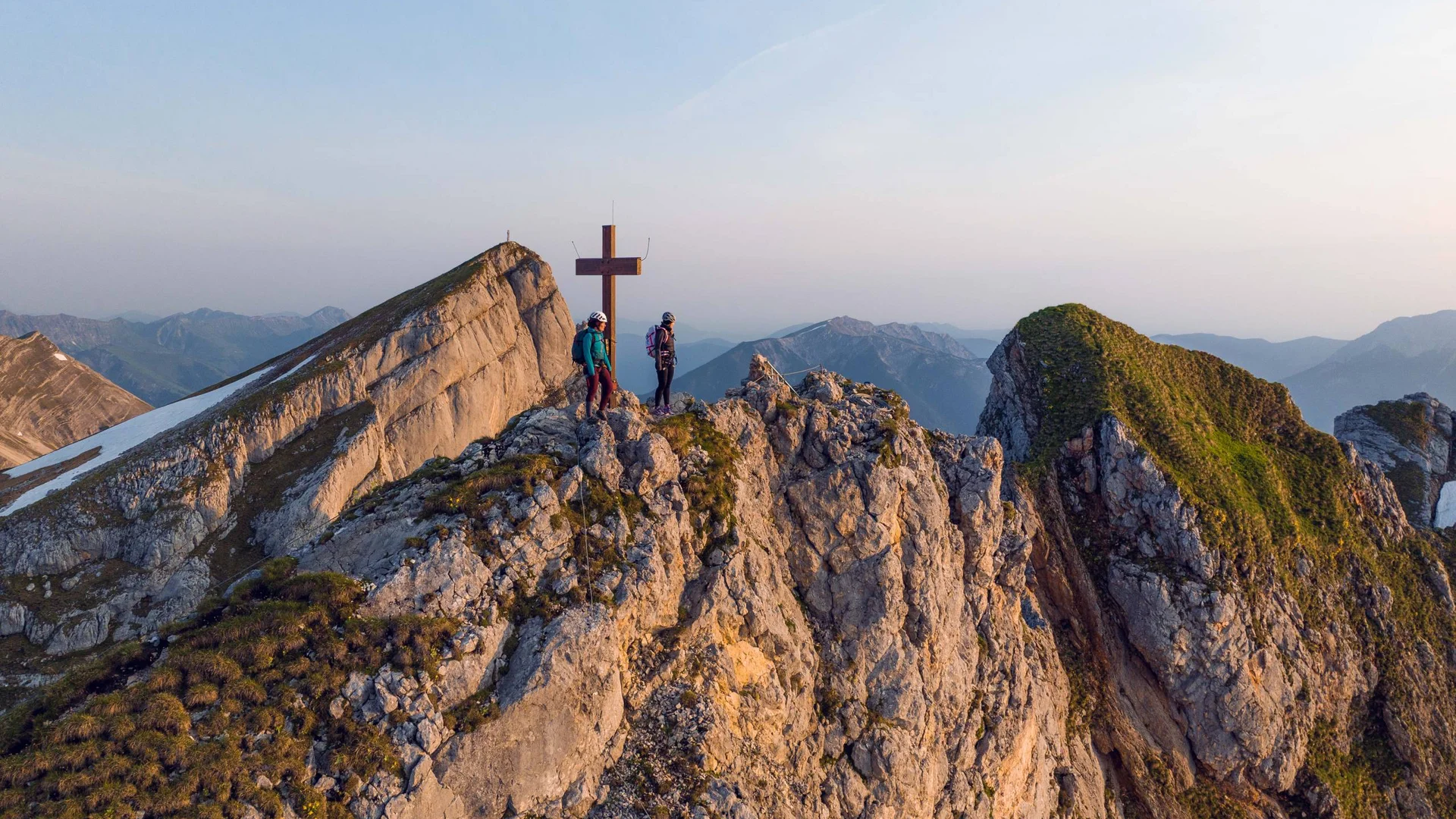 Your unforgettable active lakeside holiday in Austria Two hikers on rocky mountain summit next to summit cross at sunset
