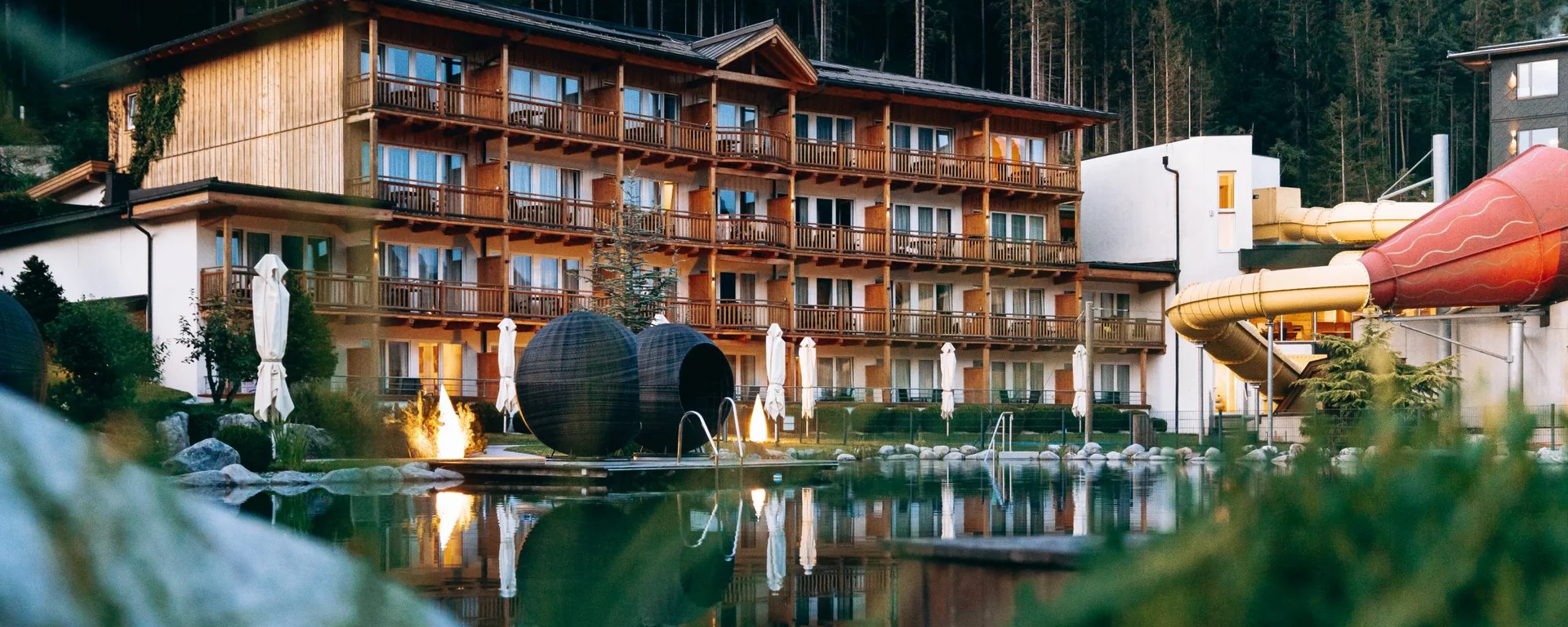 Zimmer und Angebote am Achensee Hotel mit Holzfassade und Wasserrutsche neben einem See vor Waldkulisse