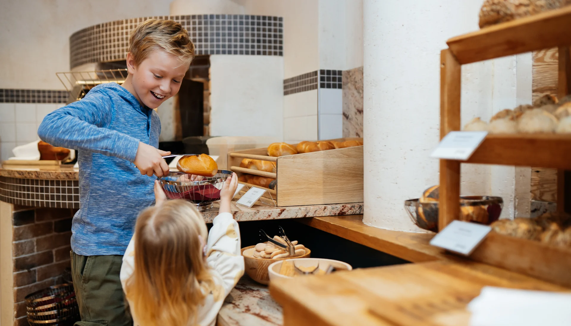 Ihr langersehnter Urlaub mit Enkelkind Junge gibt Mädchen in Bäckerei mit Zange frisches Brötchen