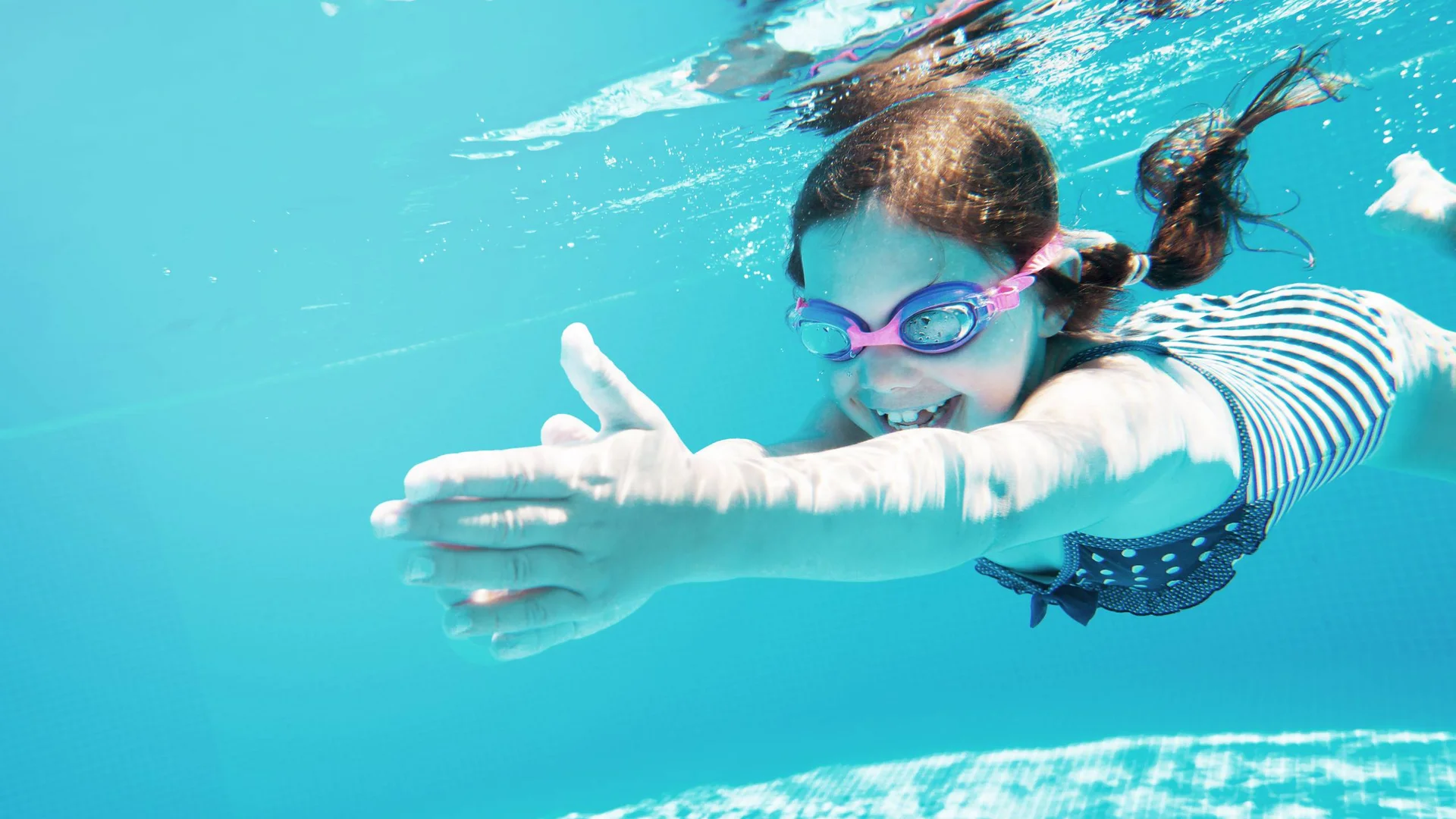 Wasserspaß im Familienhotel in Tirol mit Pool Lächendes Mädchen schwimmt unter Wasser im Pool mit Schwimmbrille und Badeanzug