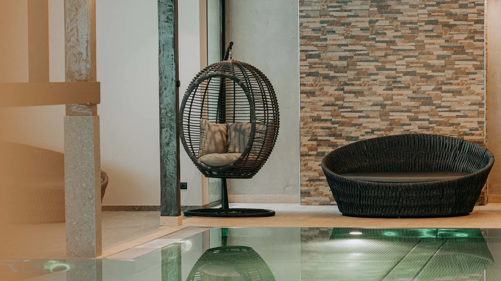 Wasserspaß im Familienhotel in Tirol mit Pool Innenpool mit runder Hängeschaukel und Korbsessel vor Steinwand