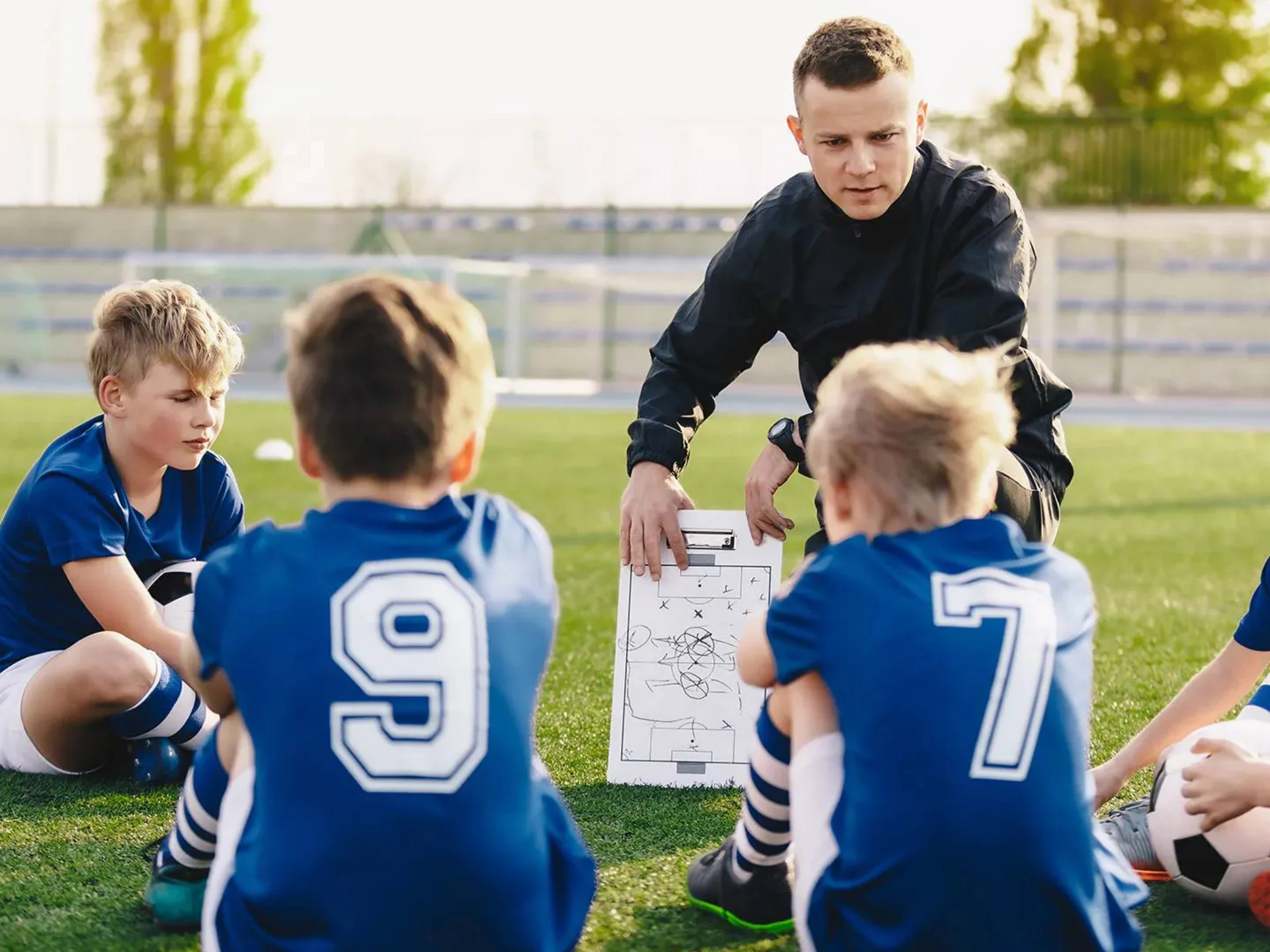 Aktiver Urlaub im Hotel mit Fußballcamp Trainer erklärt Kindern Spieltaktiken mit Taktiktafel auf Fußballfeld