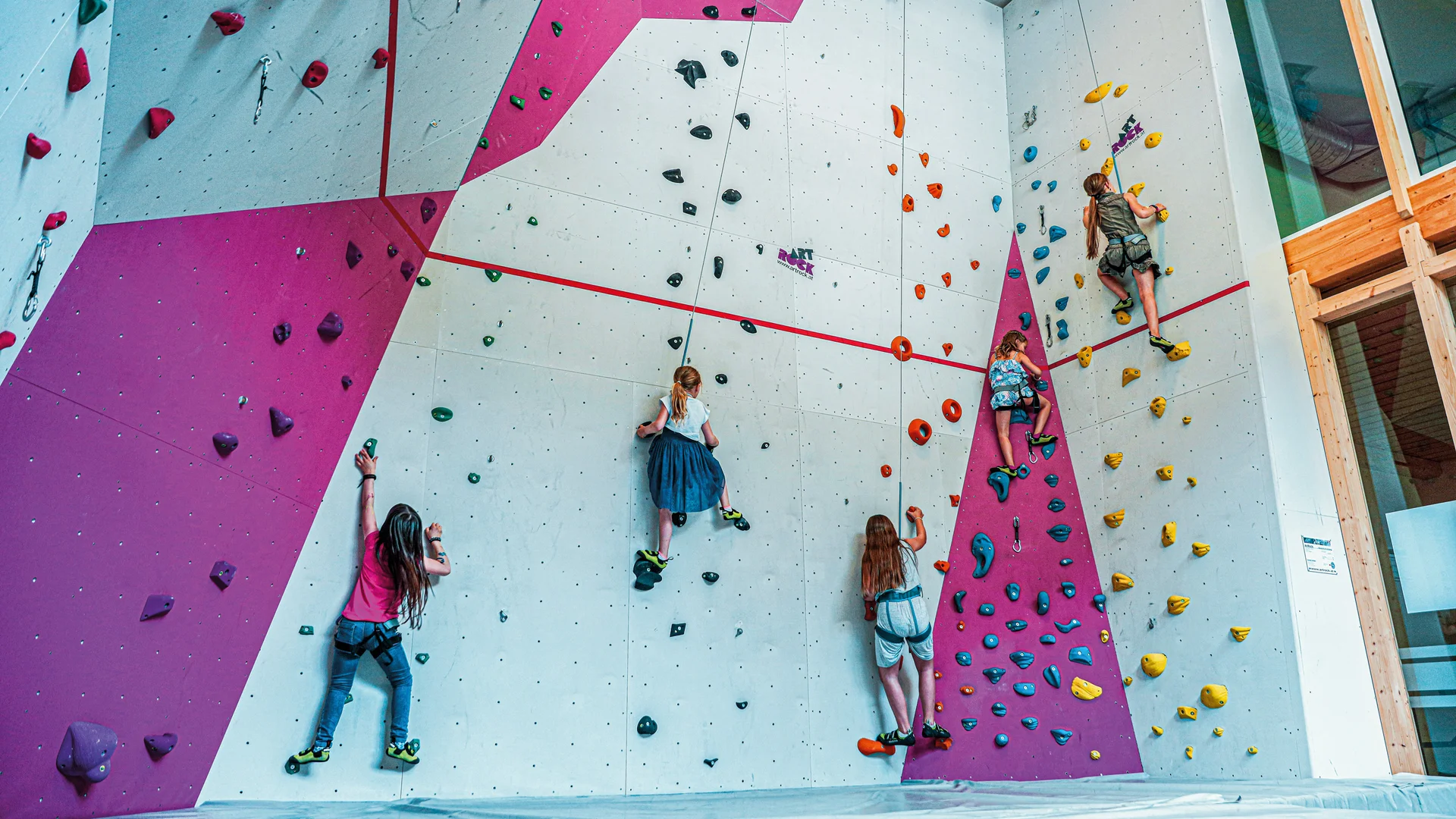 Freizeitkurse für Ihre Kids und Teenies Kinder klettern an einer bunten Indoor-Kletterwand in einer Halle
