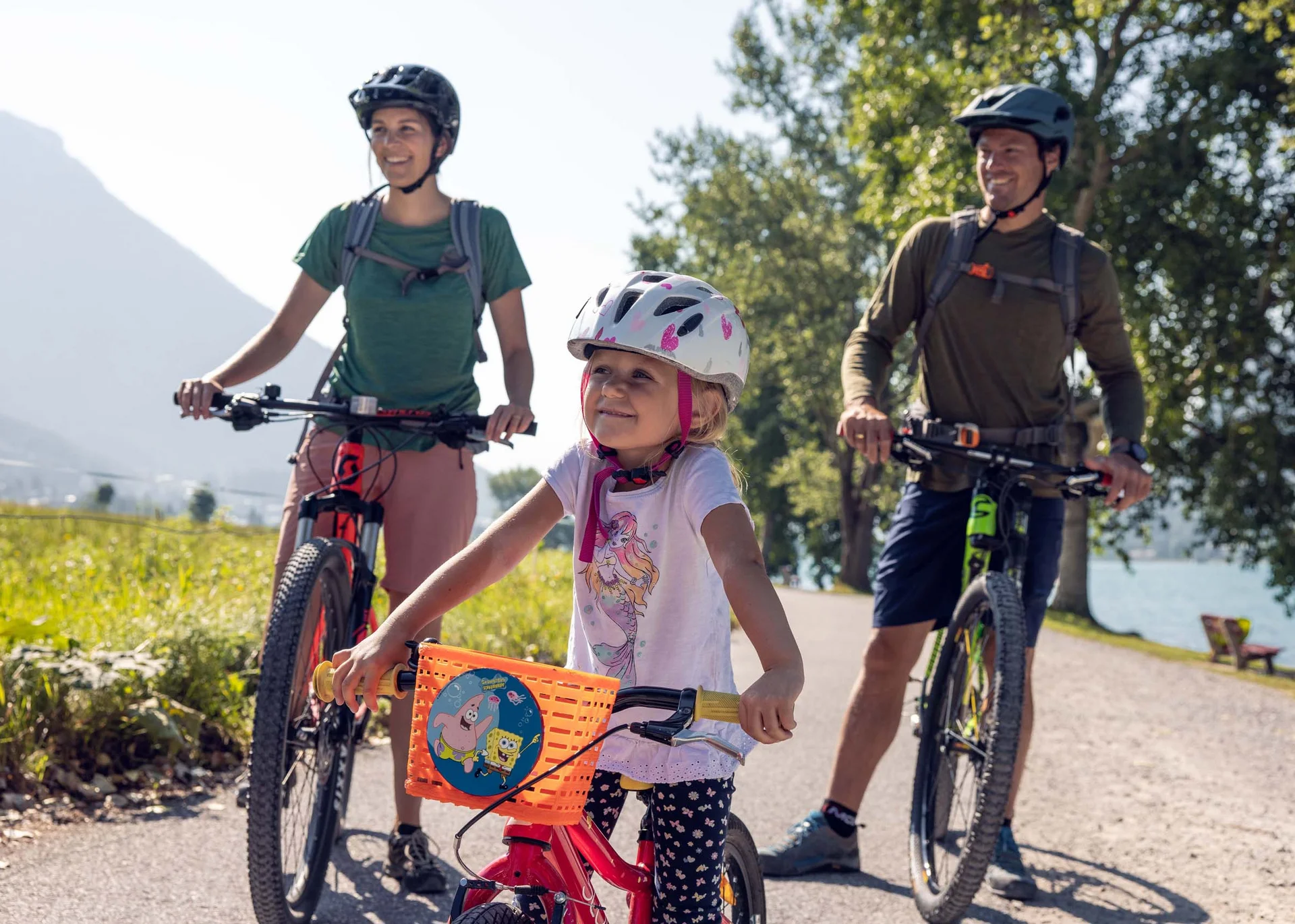 Radtouren für Groß und Klein: Ihr Bikehotel in Tirol Familie mit Kind auf Fahrradtour in sonniger Landschaft mit Bergen und See