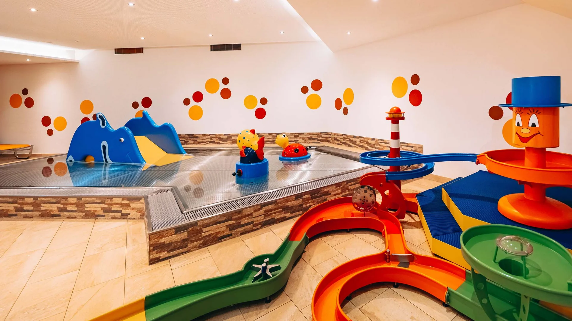 Urlaub im Hotel mit Indoorspielplatz Buntes Indoor-Kinderbecken mit Rutschen und Wasserspielzeug
