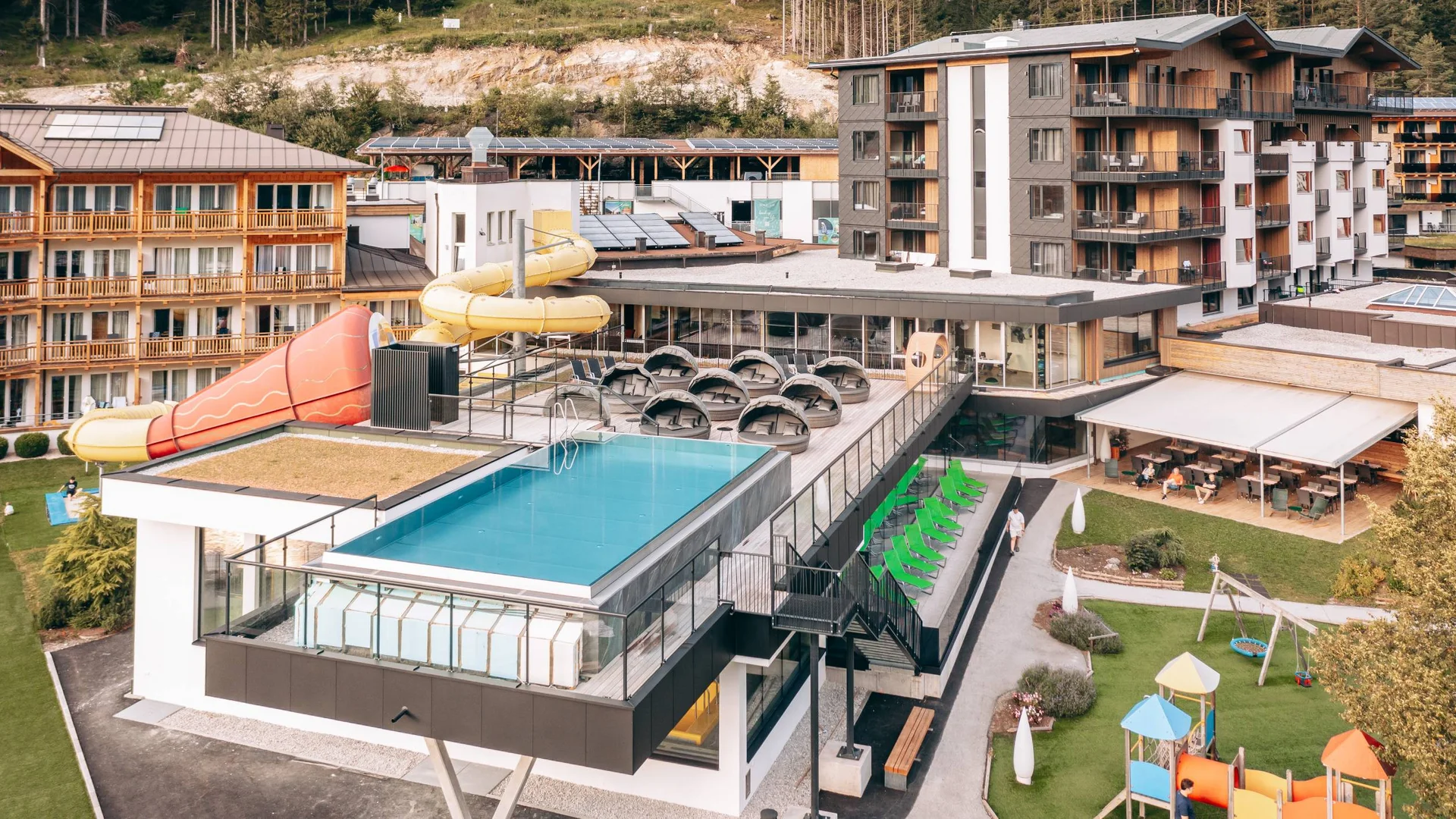 Wasserspaß im Familienhotel in Tirol mit Pool Hotel mit Außenpool, Wasserrutsche und Spielplatz in einer Berglandschaft