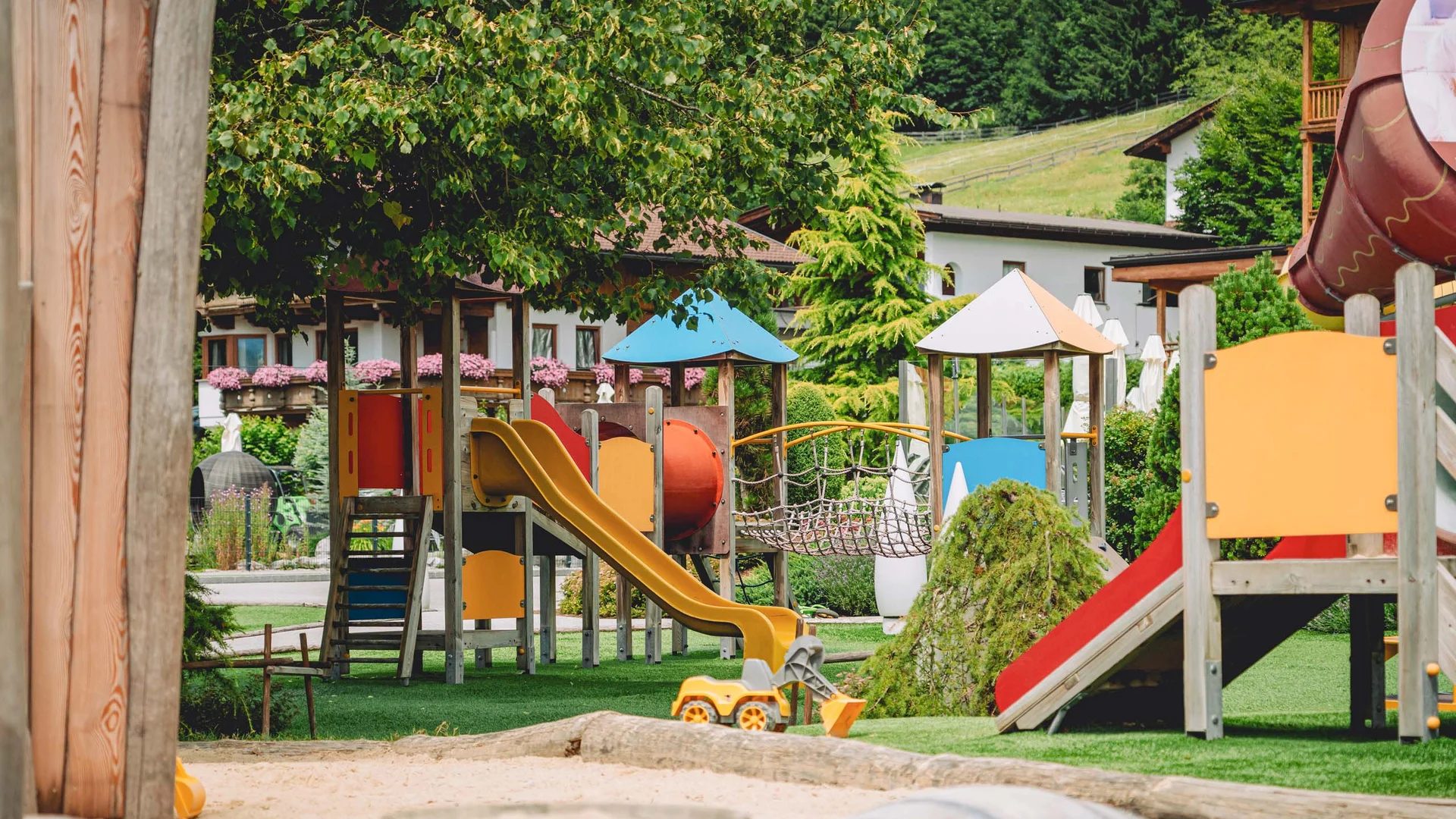 Outdoorspaß im Familienhotel am See in Österreich Kinderspielplatz mit Rutschen, Spielgeräten und Sandkasten in einem Garten