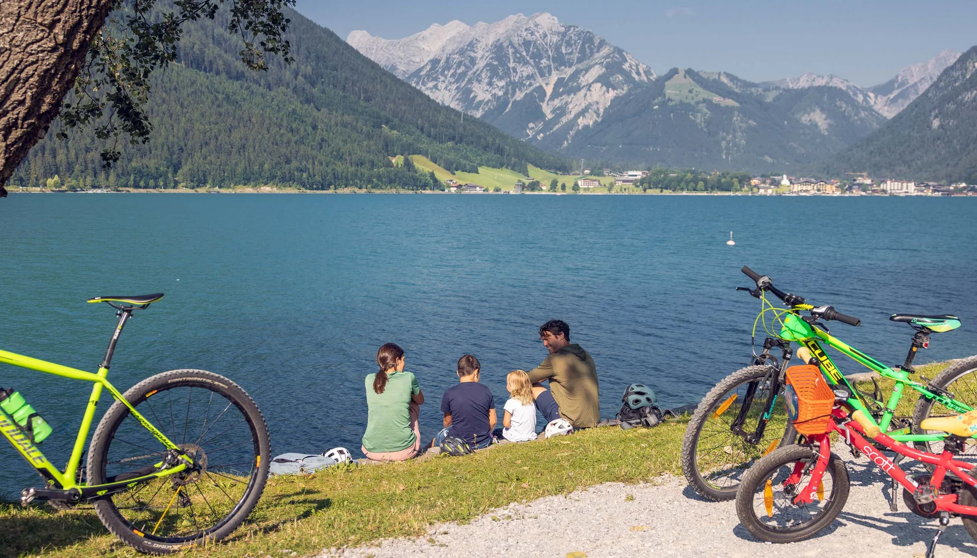 Radtouren für Groß und Klein: Ihr Bikehotel in Tirol Familie mit Fahrrädern am See vor Alpenpanorama bei Sonnenschein