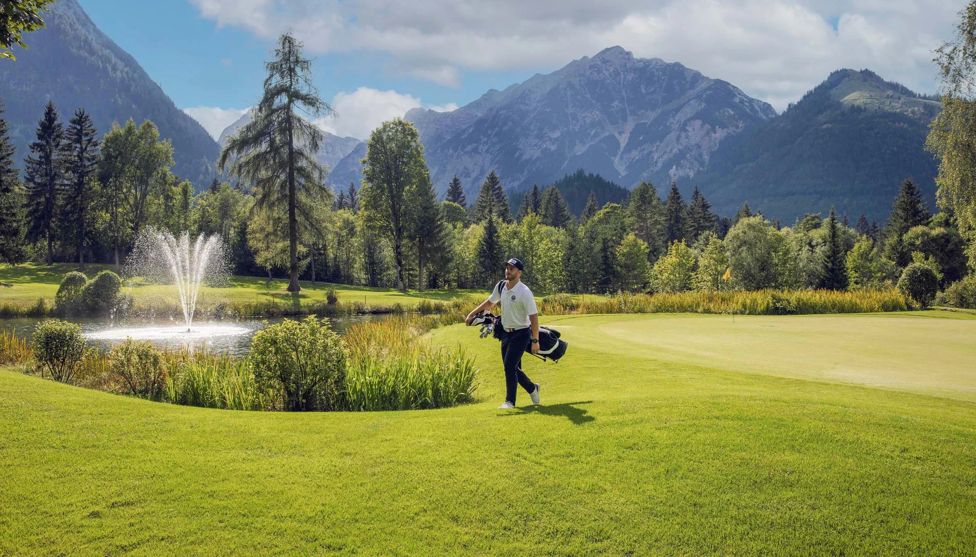 Your unforgettable active lakeside holiday in Austria Golfer walking on green course with mountains and water fountain in background