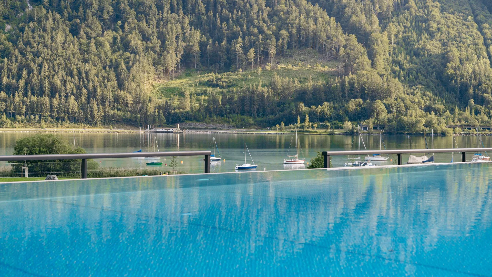 Wasserspaß im Familienhotel in Tirol mit Pool Blick auf See mit Segelbooten und bewaldeten Bergen im Hintergrund
