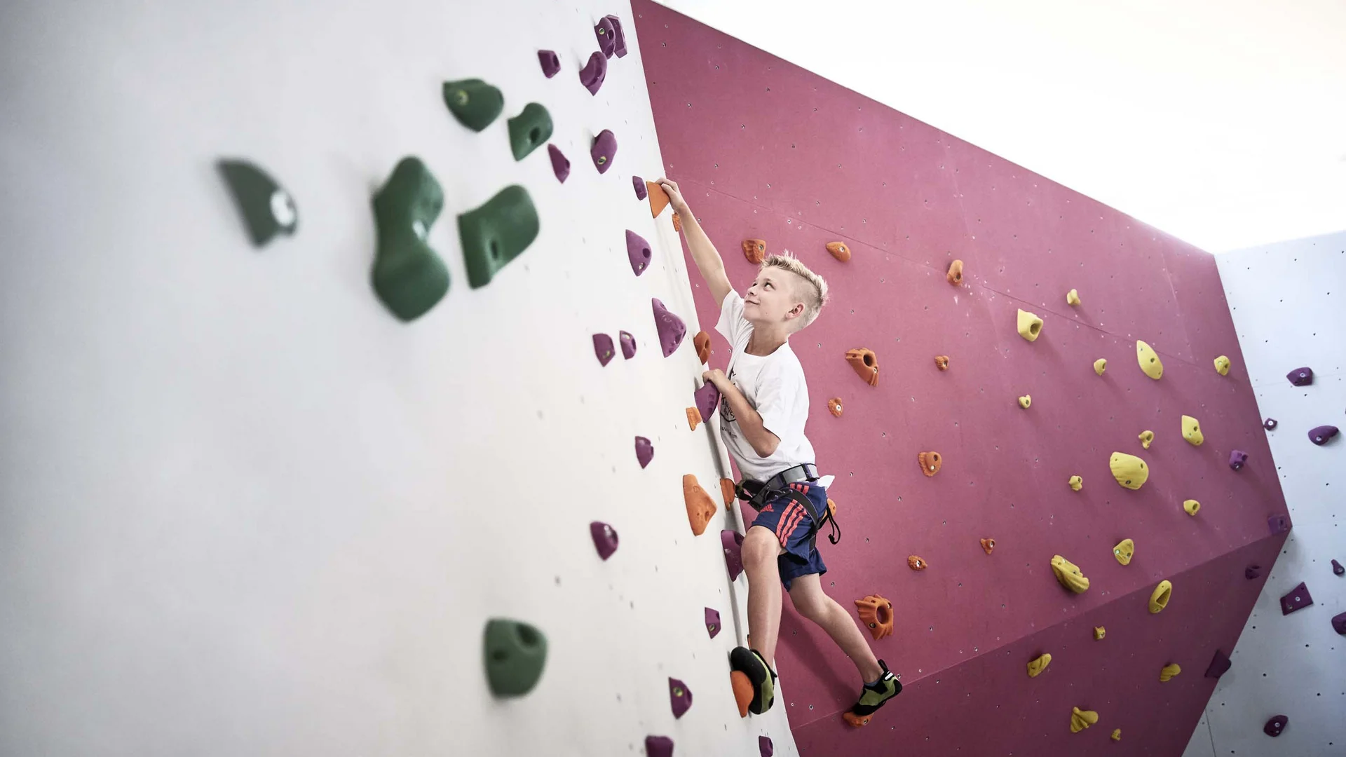 Ihr Familienhotel in Österreich mit All-inclusive-Angebot Junge beim Klettern an einer bunten Kletterwand in der Halle