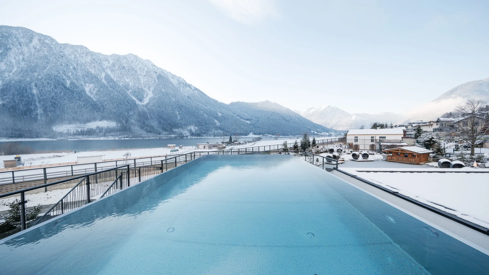 Willkommen im Familienhotel Buchau am Achensee Infinity-Pool mit Blick auf verschneite Berge und Häuser im Winter
