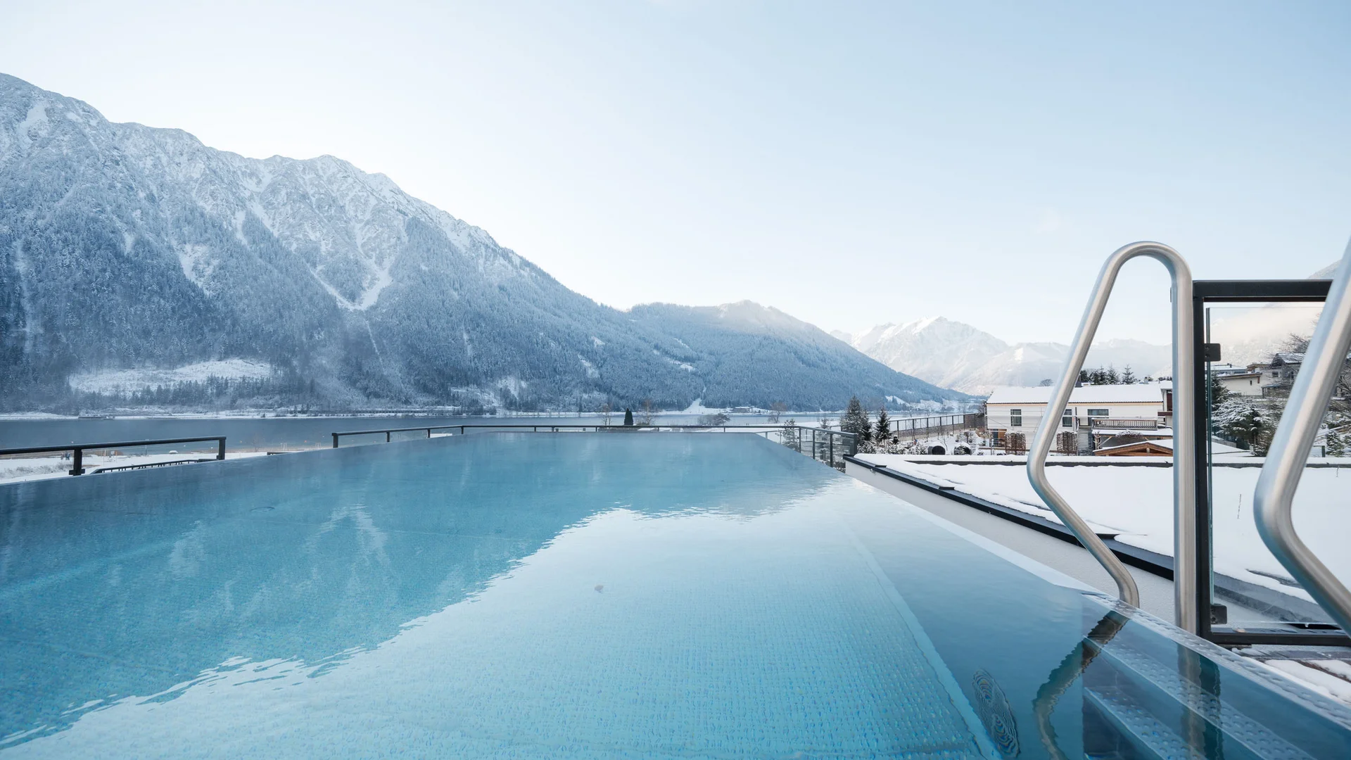 Urlaub im Wellnesshotel mit Kindern in Tirol Infinity-Pool mit Blick auf schneebedeckte Berge und einen See bei klarem Himmel