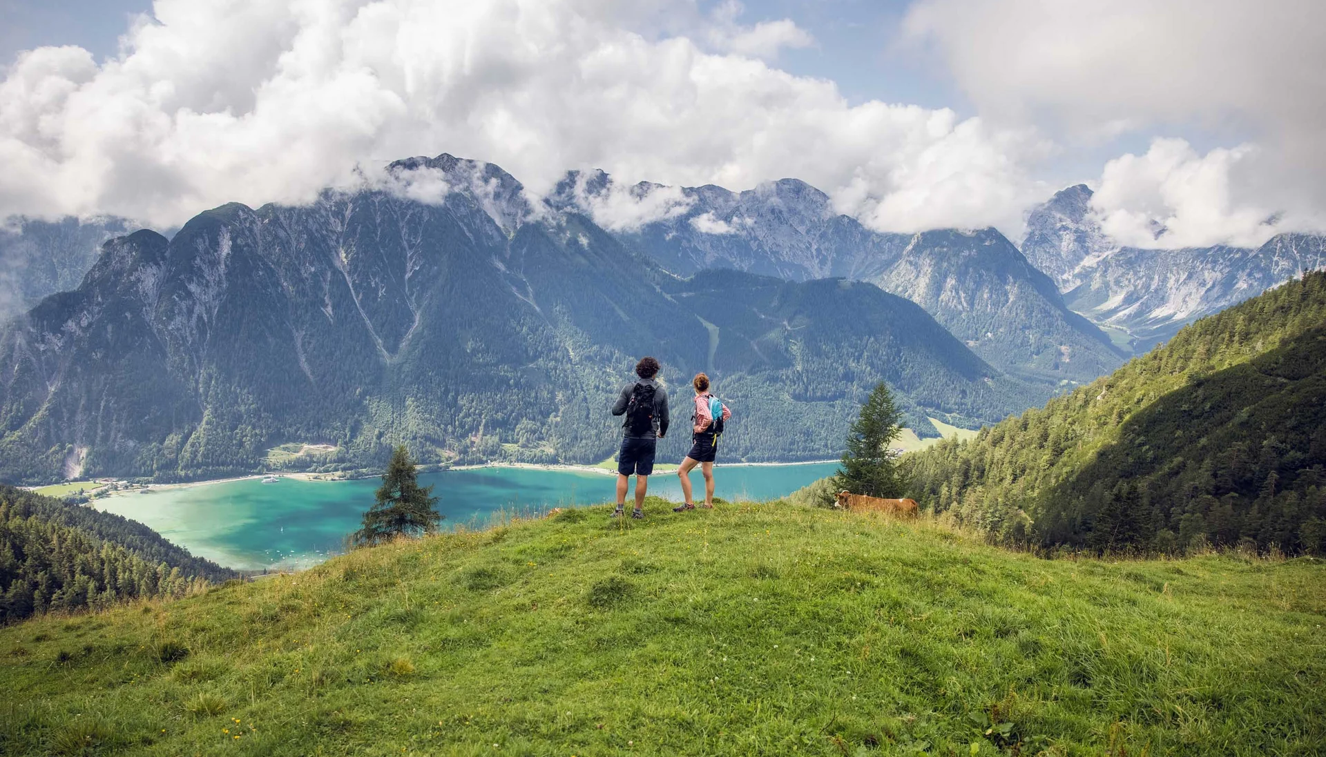 Your unforgettable active lakeside holiday in Austria Two hikers standing on grass hill overlooking mountains and lake