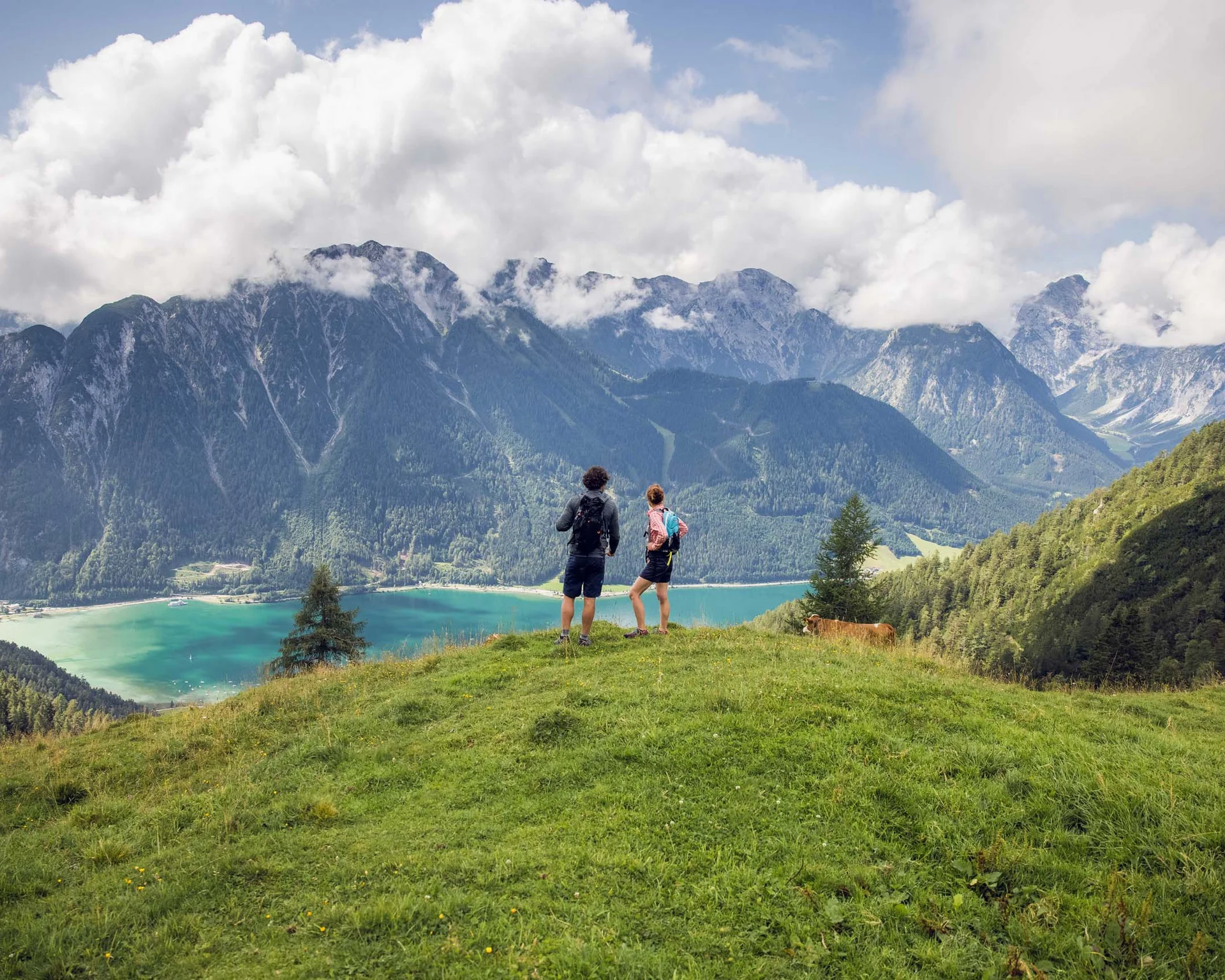 Erholungsurlaub für Eltern Zwei Wanderer stehen auf einer Wiese mit Berg- und Seeblick