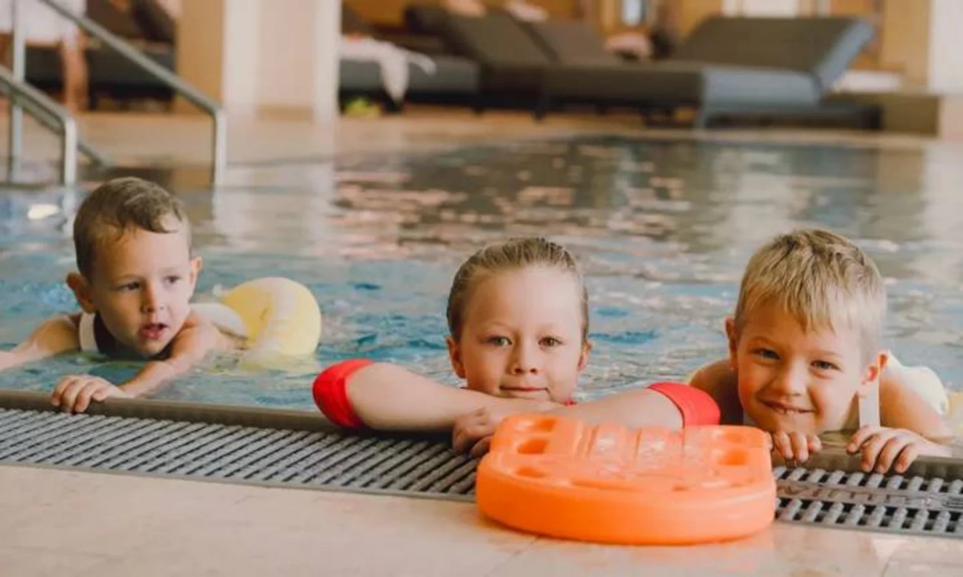 Familienurlaub mit Baby und Kleinkind im Buchau Drei Kinder im Hallenbad am Beckenrand mit Schwimmhilfen