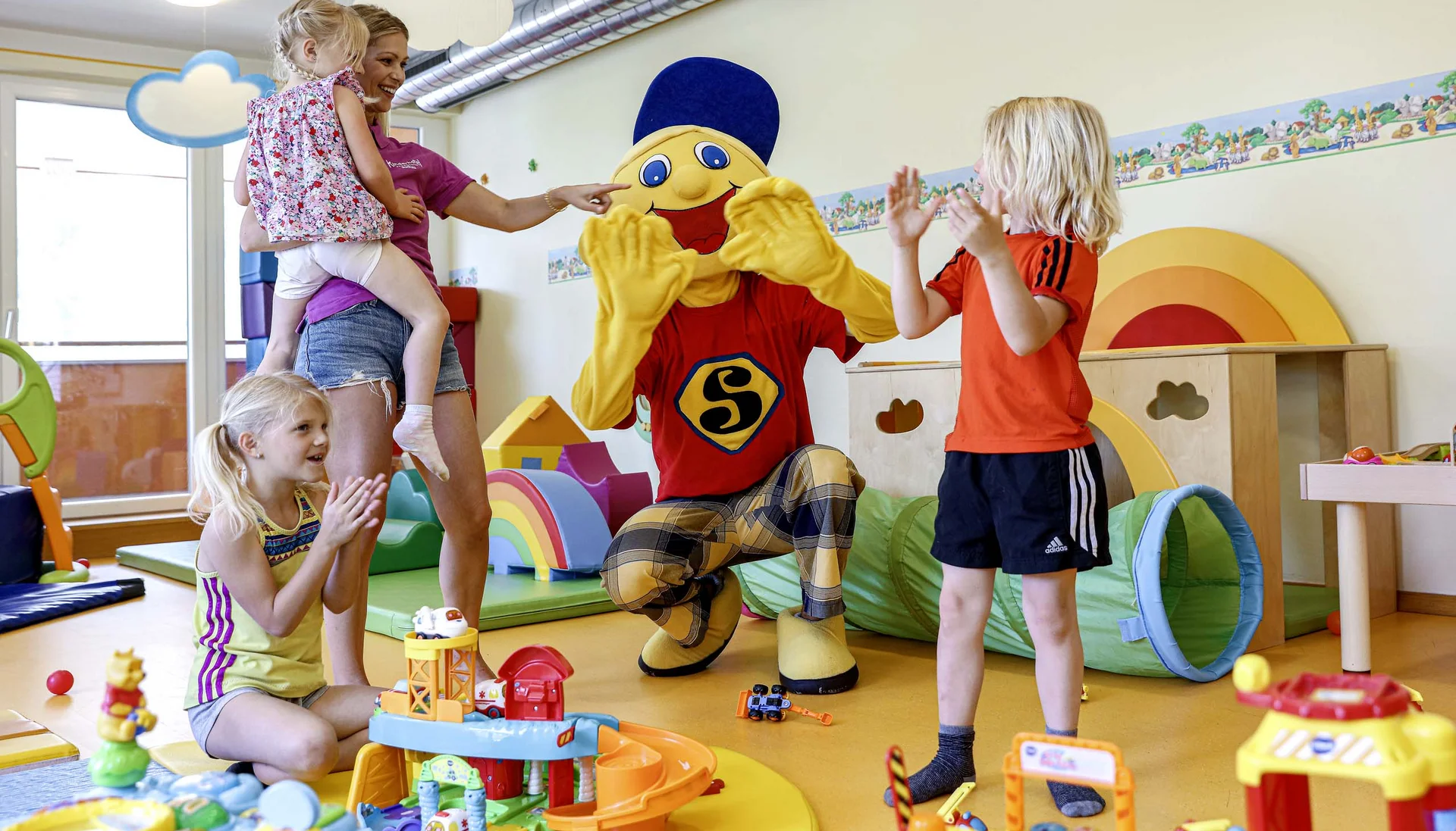Ihr Familienhotel in Österreich mit All-inclusive-Angebot Kinder spielen und klatschen mit einer Person in einem bunten Maskottchenkostüm in einem Spielzimmer