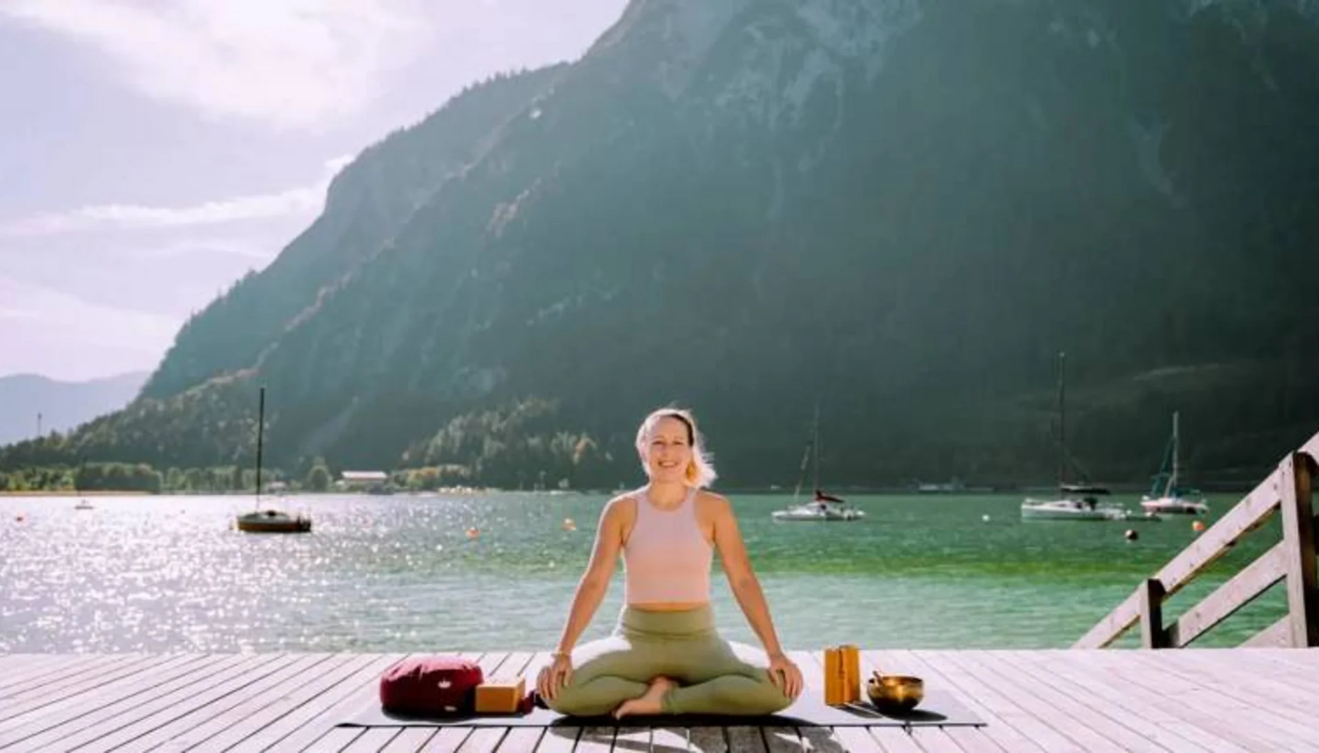 Fitness und Yoga im Hotel in Tirol Frau macht Yoga auf Steg am See mit Bergen und Booten im Hintergrund