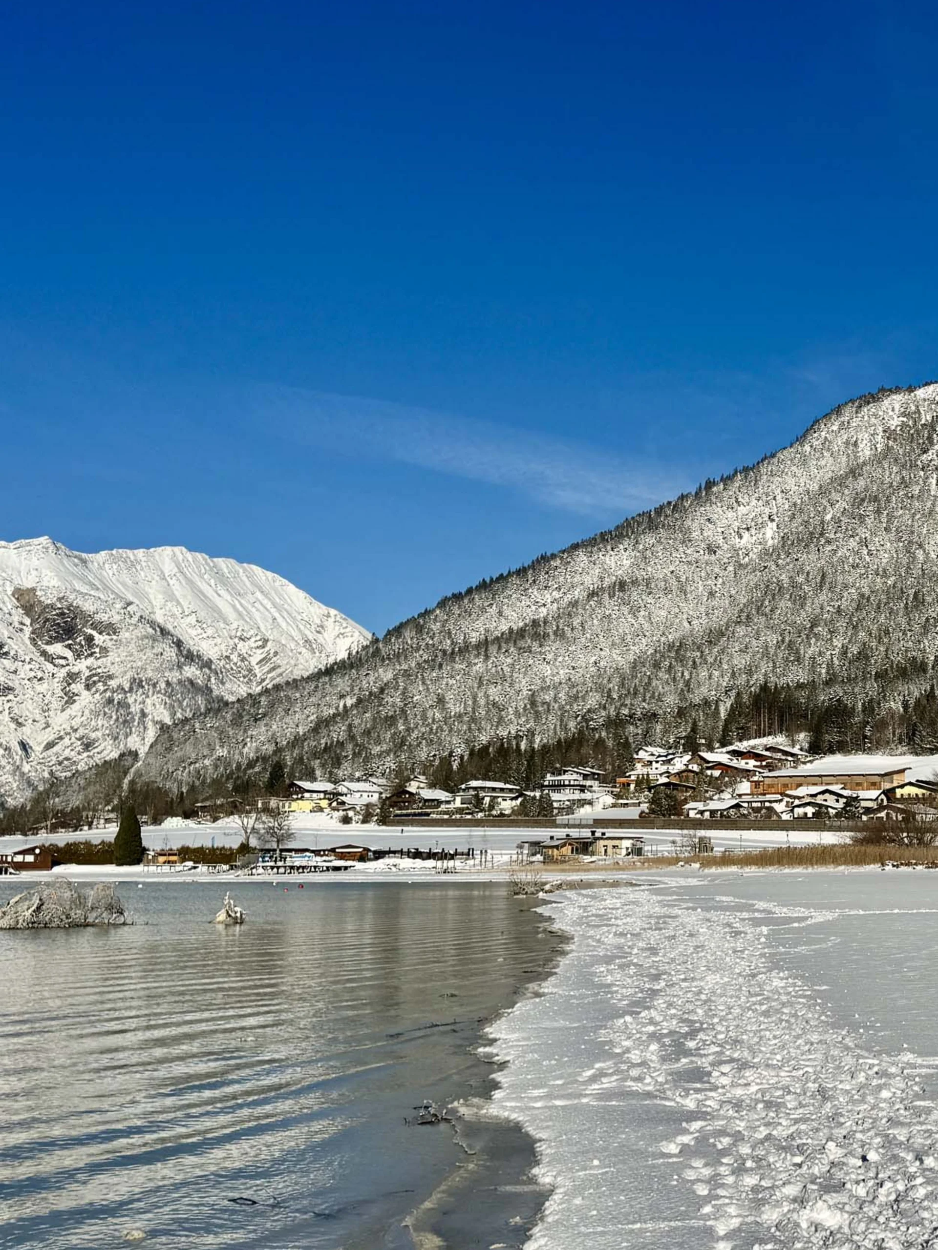 Urlaub im Familienresort in Österreich Verschneite Berglandschaft mit Dorf am gefrorenen See unter klarem blauen Himmel