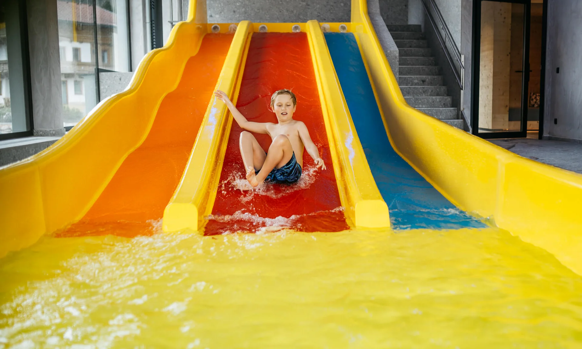 Welcome to our family hotel at Lake Achensee. Child sliding down red water slide into pool in indoor water park