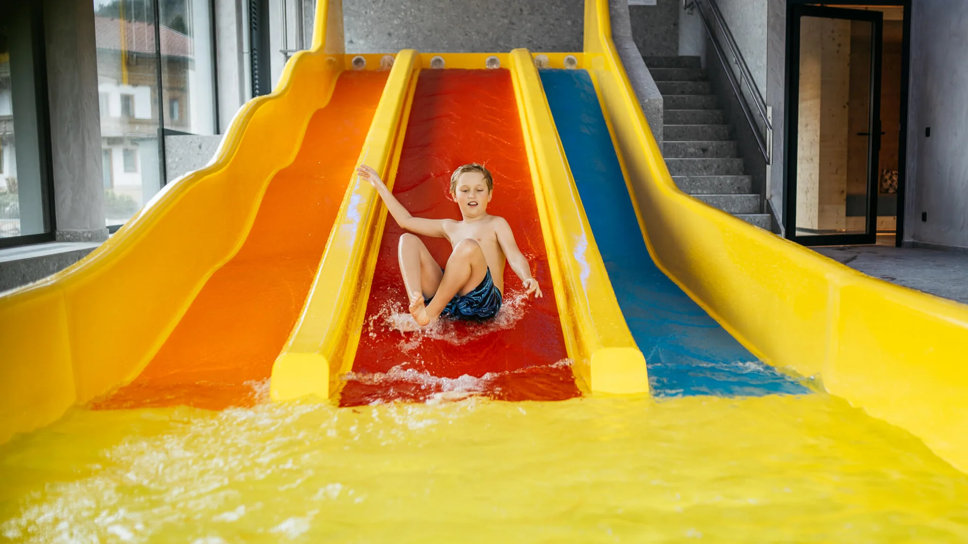 Urlaub im Hotel mit Indoorspielplatz Kind rutscht auf roter Wasserrutsche in Hallenbad ins Wasser