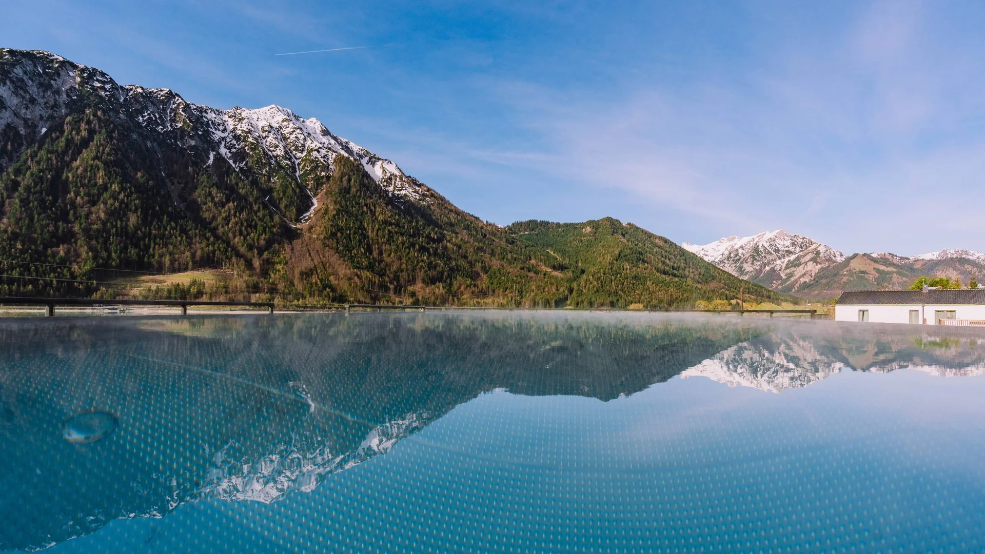 Urlaub im Wellnesshotel mit Kindern in Tirol Berglandschaft mit schneebedeckten Gipfeln spiegelt sich in einem ruhigen Pool