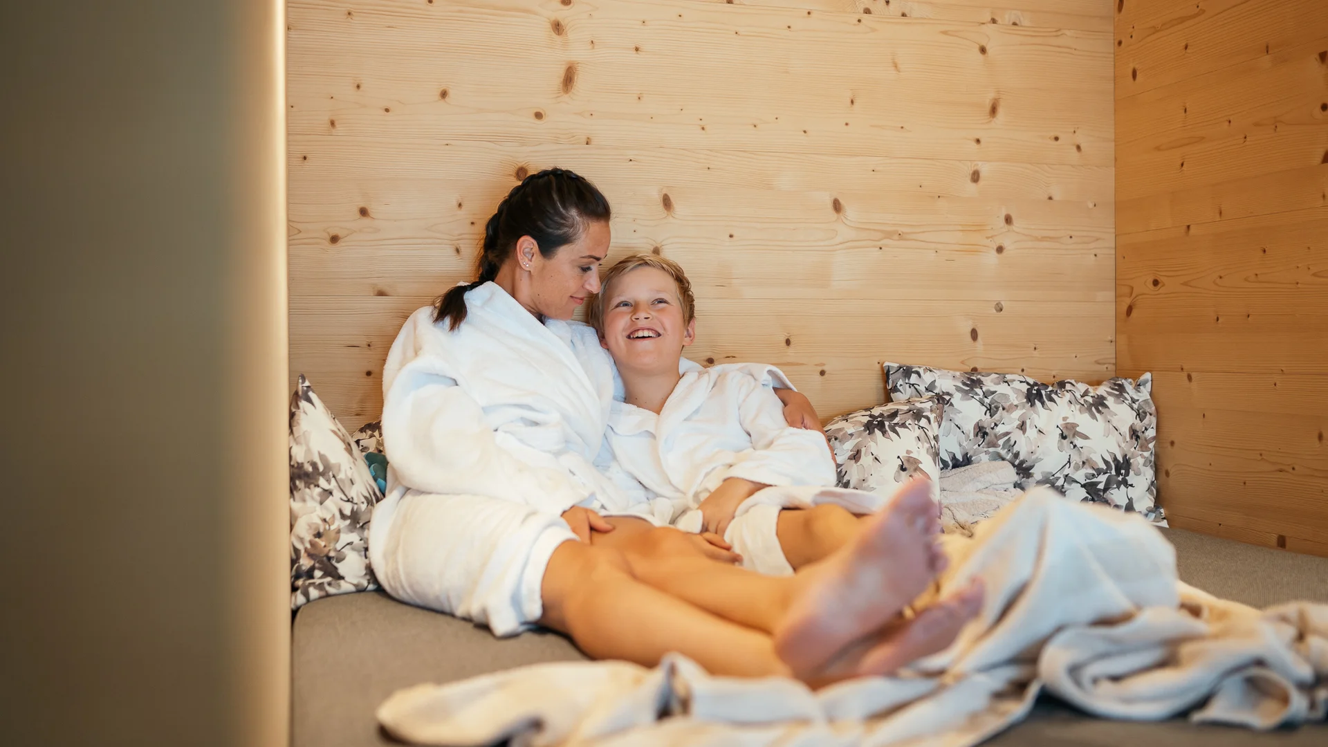 Ihr Hotel für Alleinerziehende Frau und Junge in Bademänteln entspannen auf Sofa in gemütlichem Raum