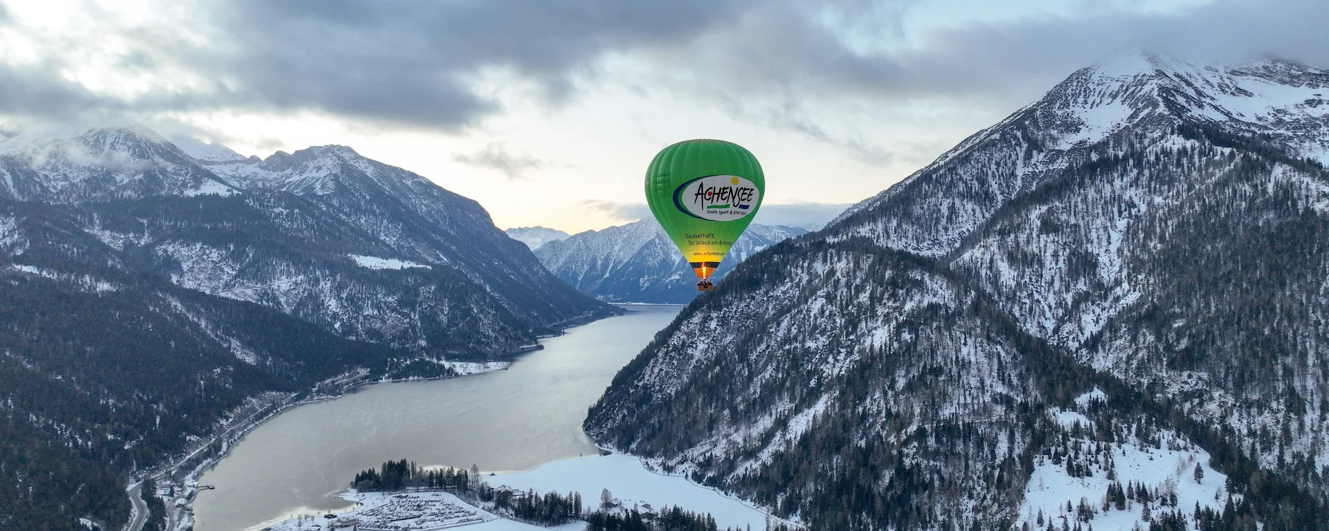 Your unforgettable active lakeside holiday in Austria Green hot air balloon over snowy valley with mountains and river