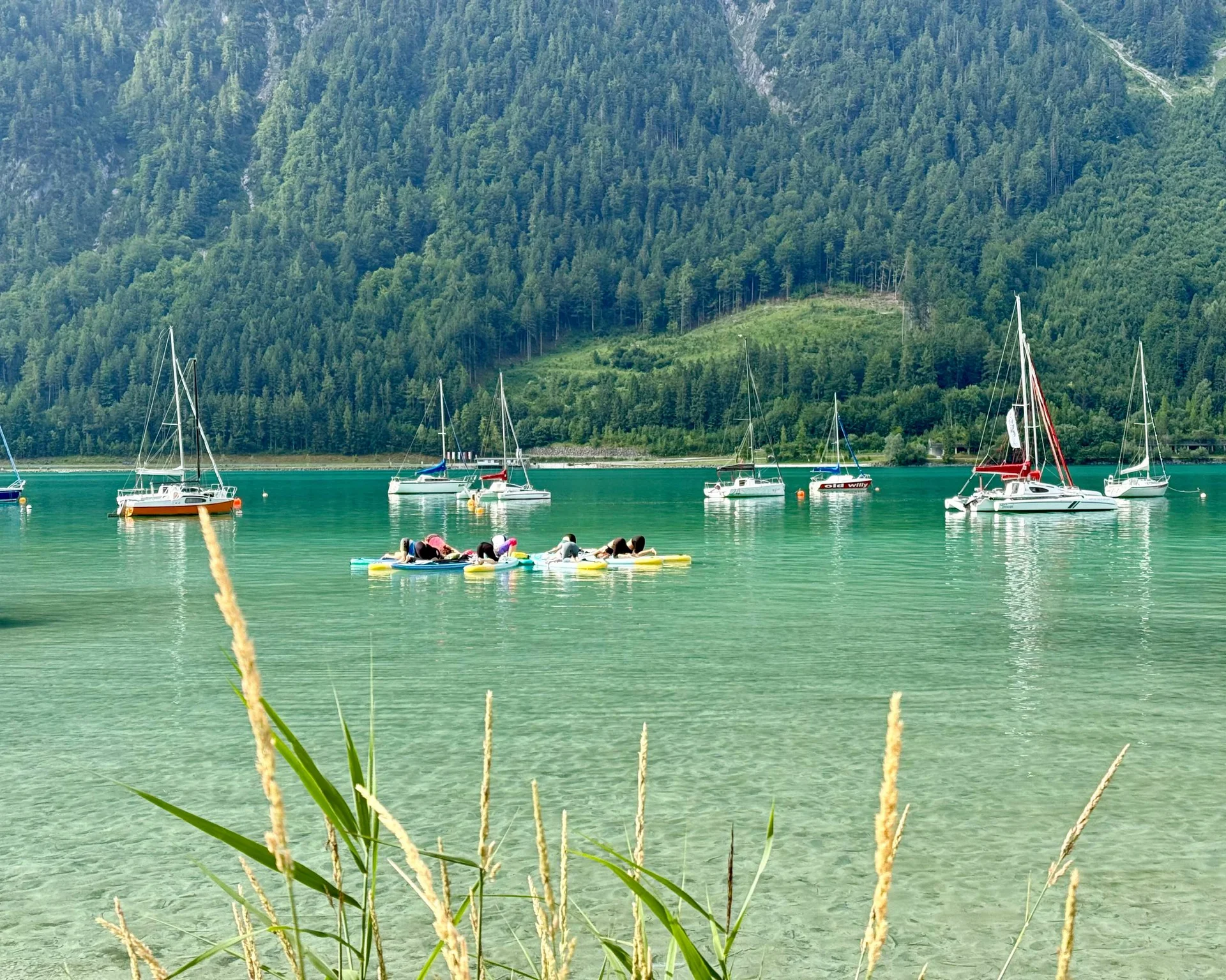 Fitness und Yoga im Hotel in Tirol Segelboote und Menschen auf dem Wasser vor bewaldetem Berg