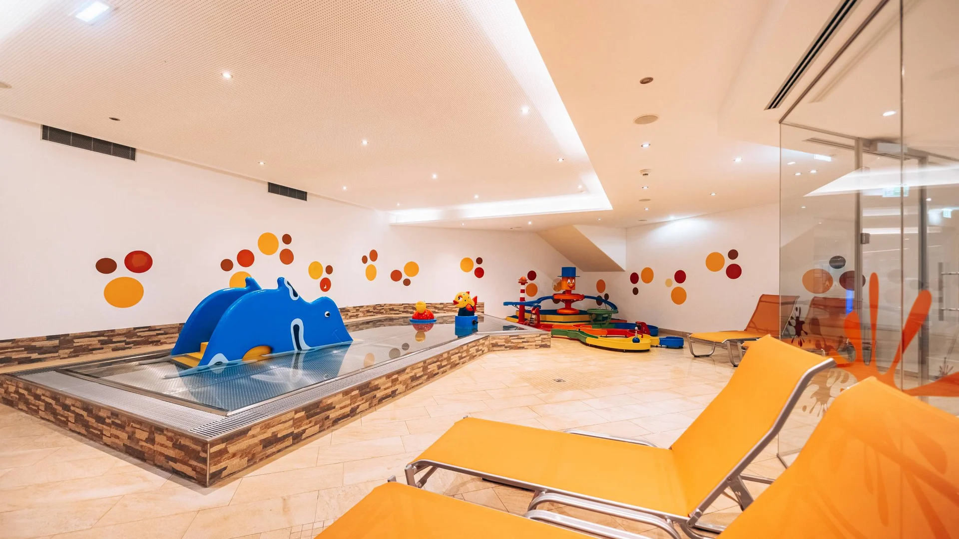 Wasserspaß im Familienhotel in Tirol mit Pool Kinderbereich mit buntem kleinen Planschbecken und orangen Liegestühlen