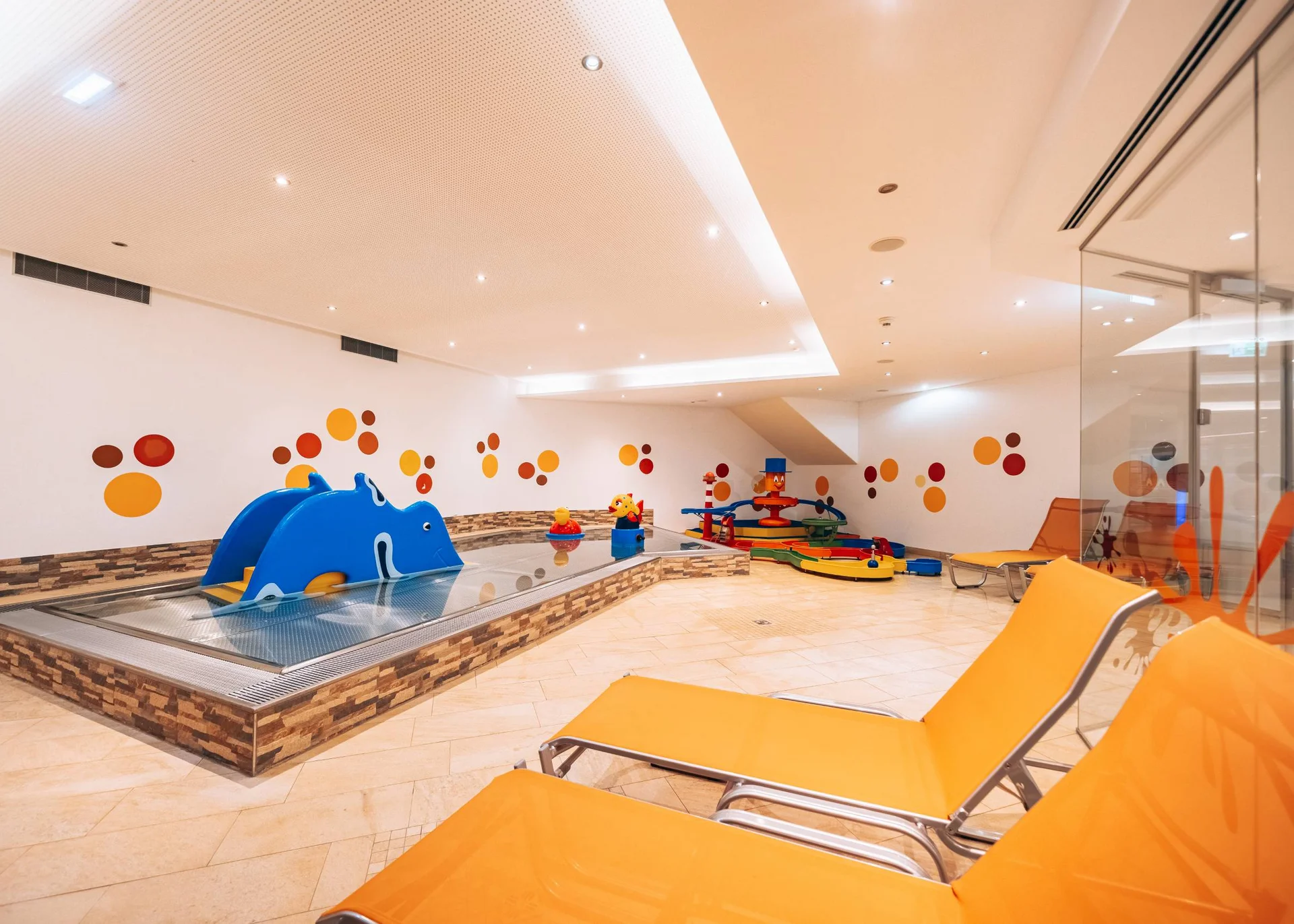 Urlaub im Wellnesshotel mit Kindern in Tirol Kinderbereich mit buntem kleinen Planschbecken und orangen Liegestühlen
