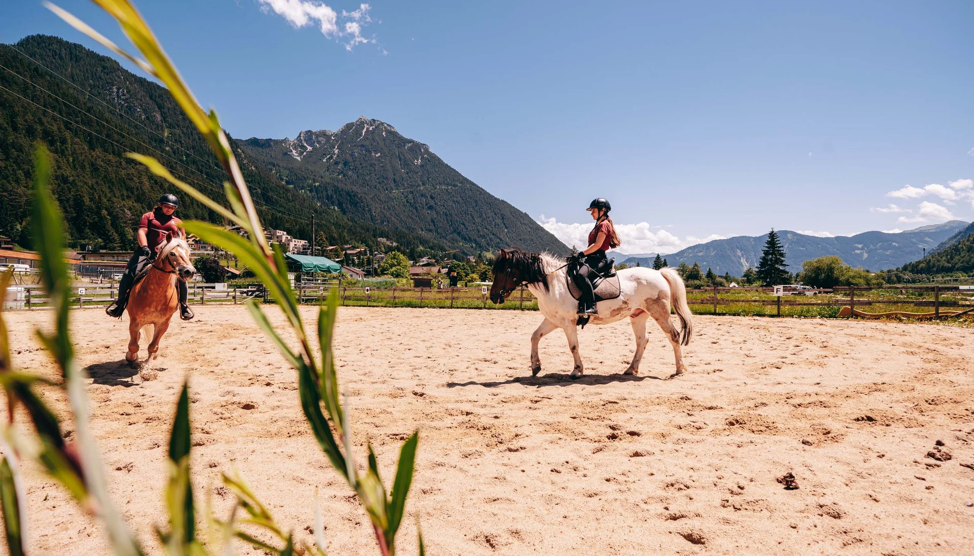 Pferdeglück im Reithotel in Österreich Zwei Reiter auf Pferden auf einem Sandplatz mit Bergen im Hintergrund