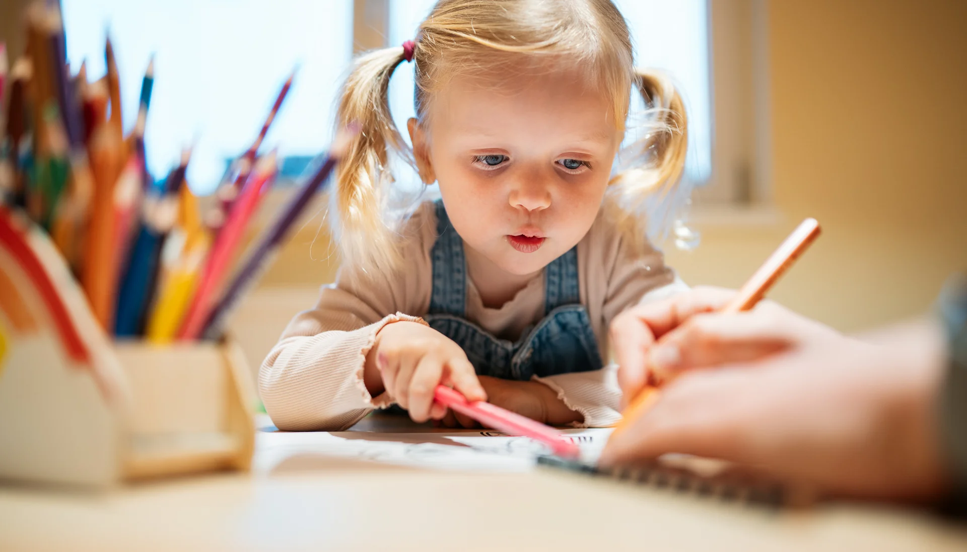 Ihr langersehnter Urlaub mit Enkelkind Kleines Mädchen malt konzentriert mit Buntstiften an einem Tisch