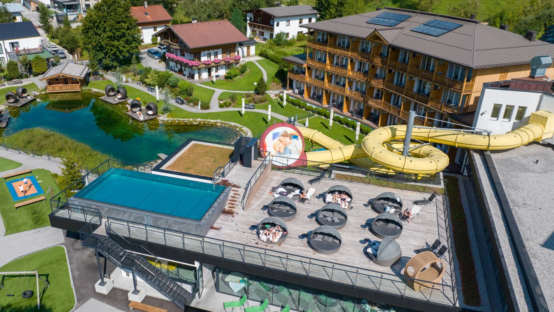 Urlaub im Hotel mit Indoorspielplatz Luftaufnahme eines Hotels mit Liegefläche, Wasserrutsche und Teich im Garten