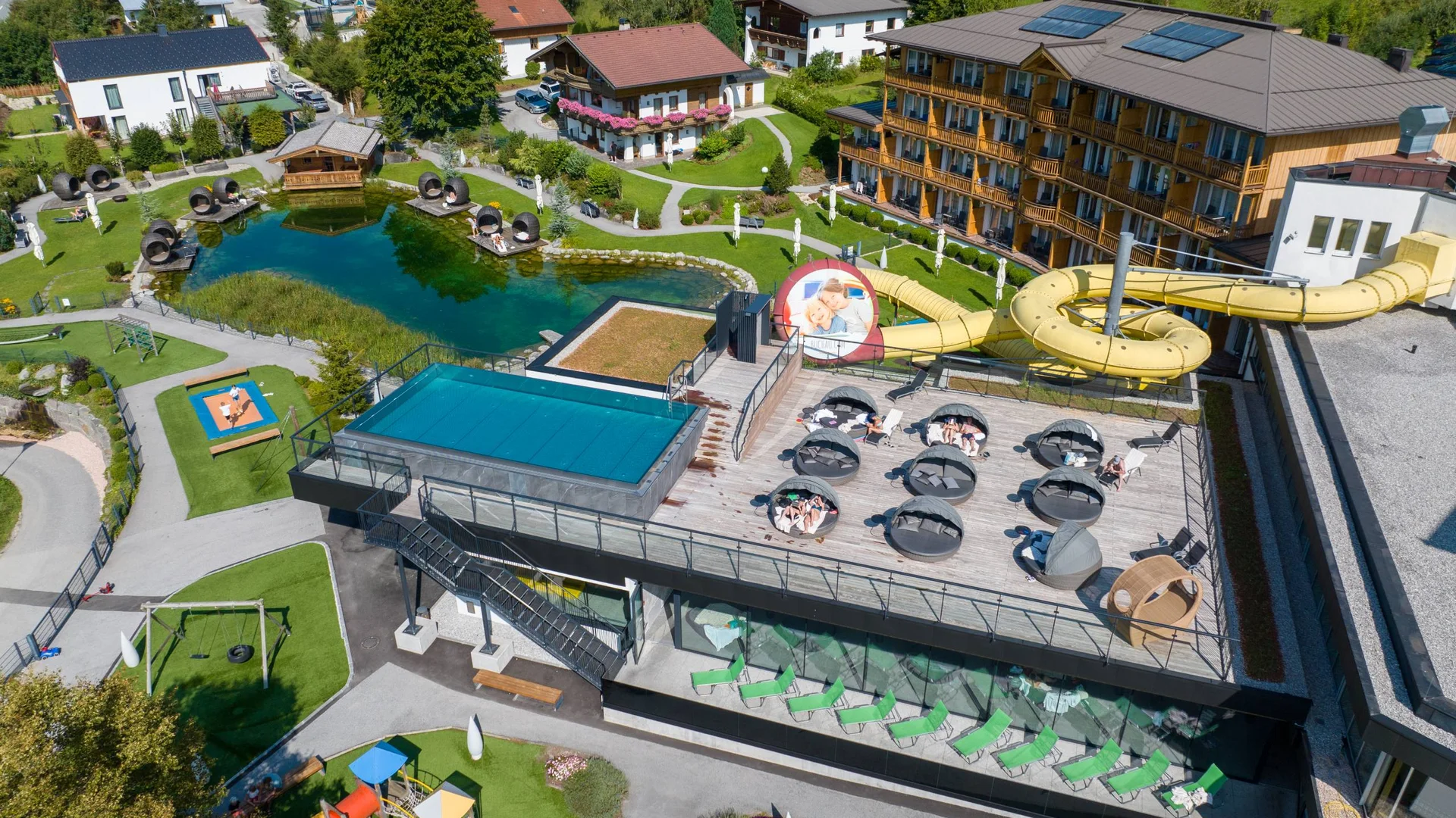 Urlaub im Wellnesshotel mit Kindern in Tirol Luftaufnahme eines Hotels mit Liegefläche, Wasserrutsche und Teich im Garten
