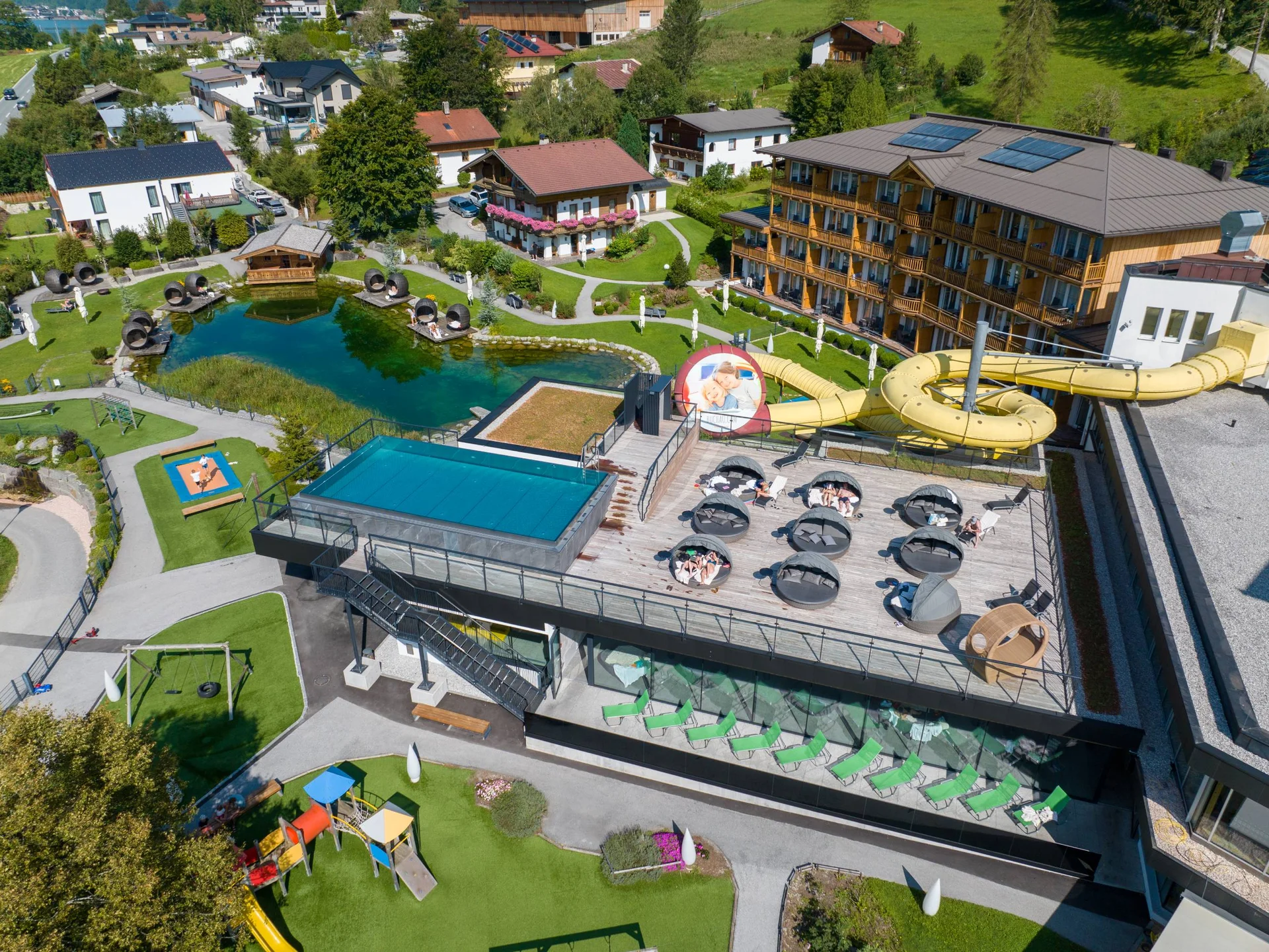 Familienzeit im Kinderhotel Buchau am Achensee Luftaufnahme eines Hotels mit Liegefläche, Wasserrutsche und Teich im Garten