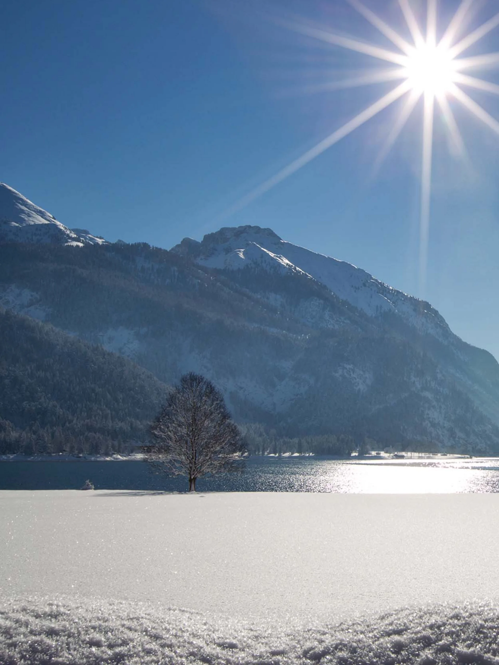 Urlaub im Familienresort in Österreich Schneebedeckter Bergsee bei Sonnenschein mit Bergen und blauem Himmel