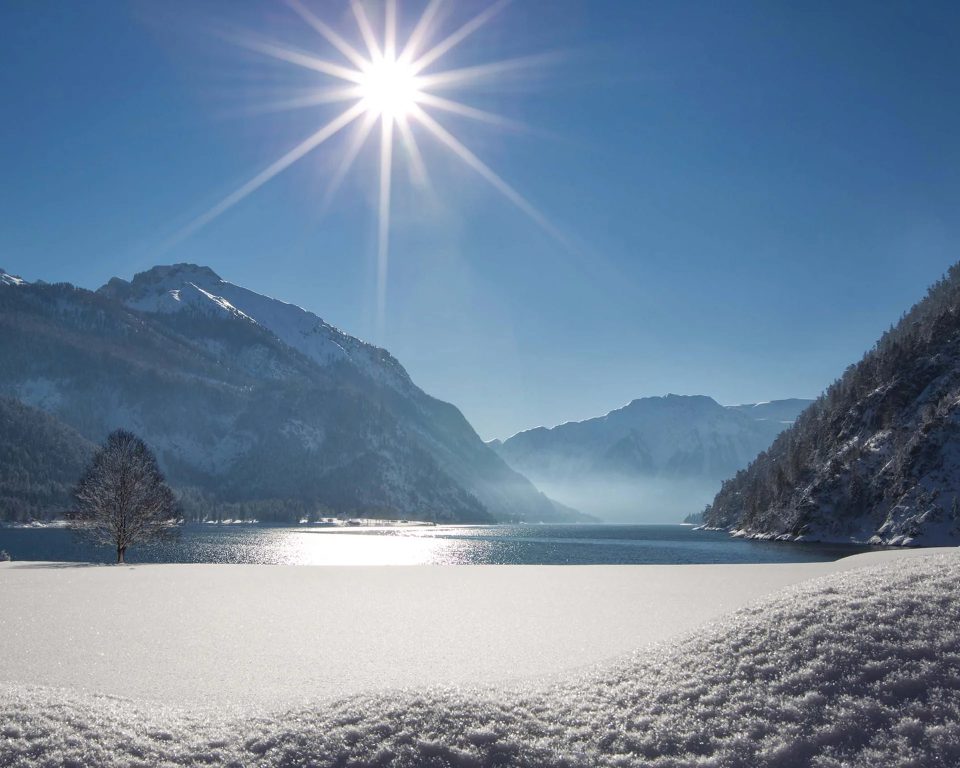 Ihr abenteuerlicher Erlebnisurlaub in Österreich Schneebedeckter Bergsee bei Sonnenschein mit Bergen und blauem Himmel