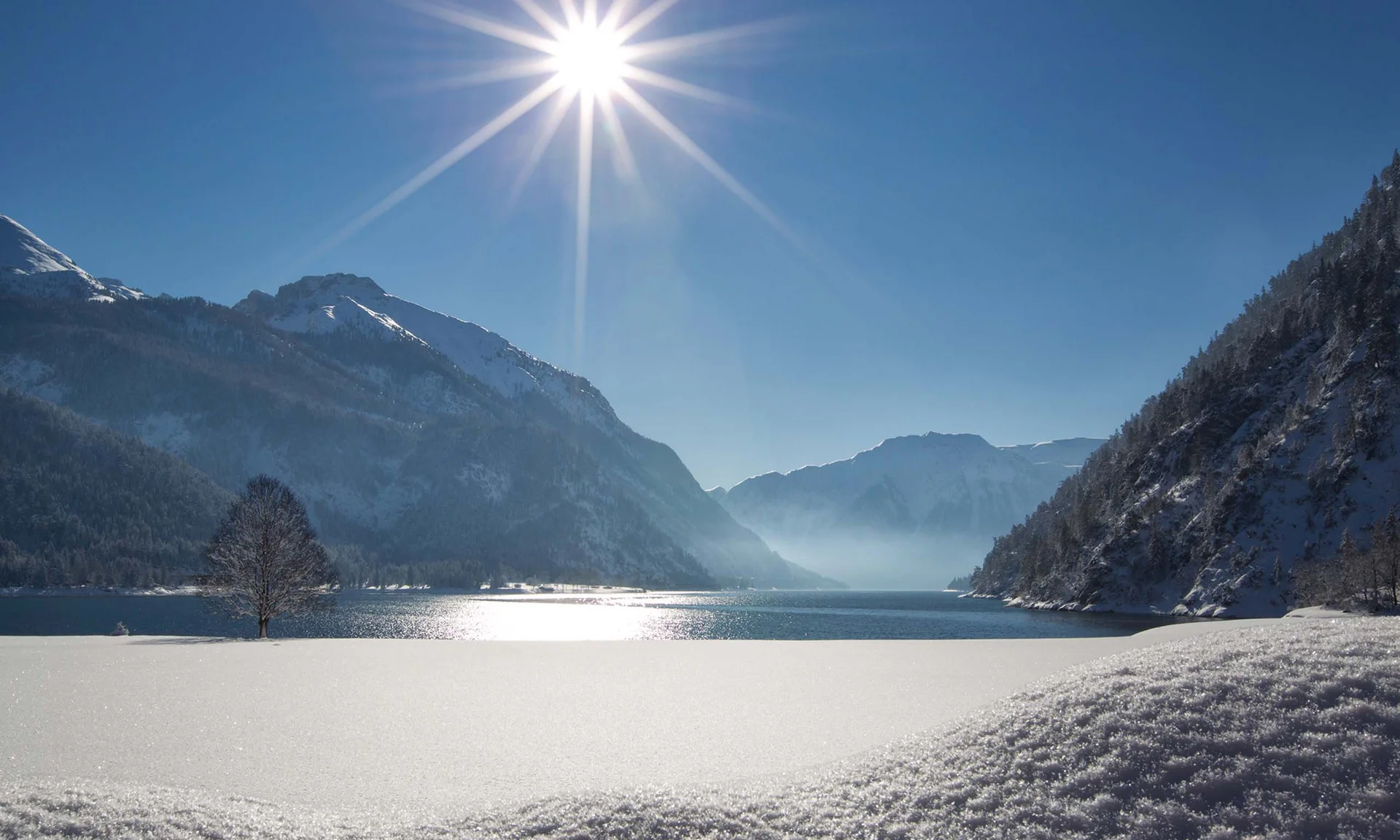 Your unforgettable active lakeside holiday in Austria Snow-covered mountain lake under bright sun with mountains and clear blue sky