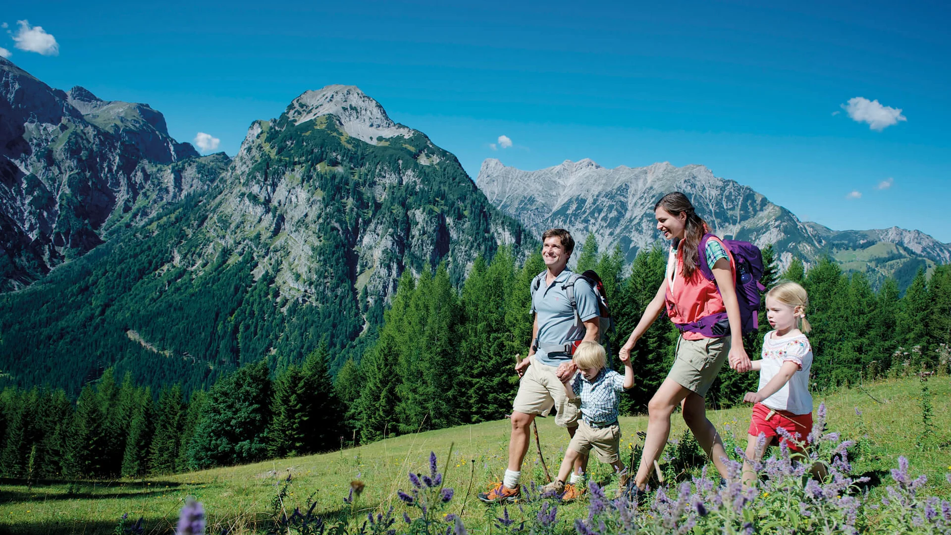 Vom Wanderhotel in Tirol direkt in die Natur Familie wandert in den Bergen bei sonnigem Wetter mit blühender Wiese