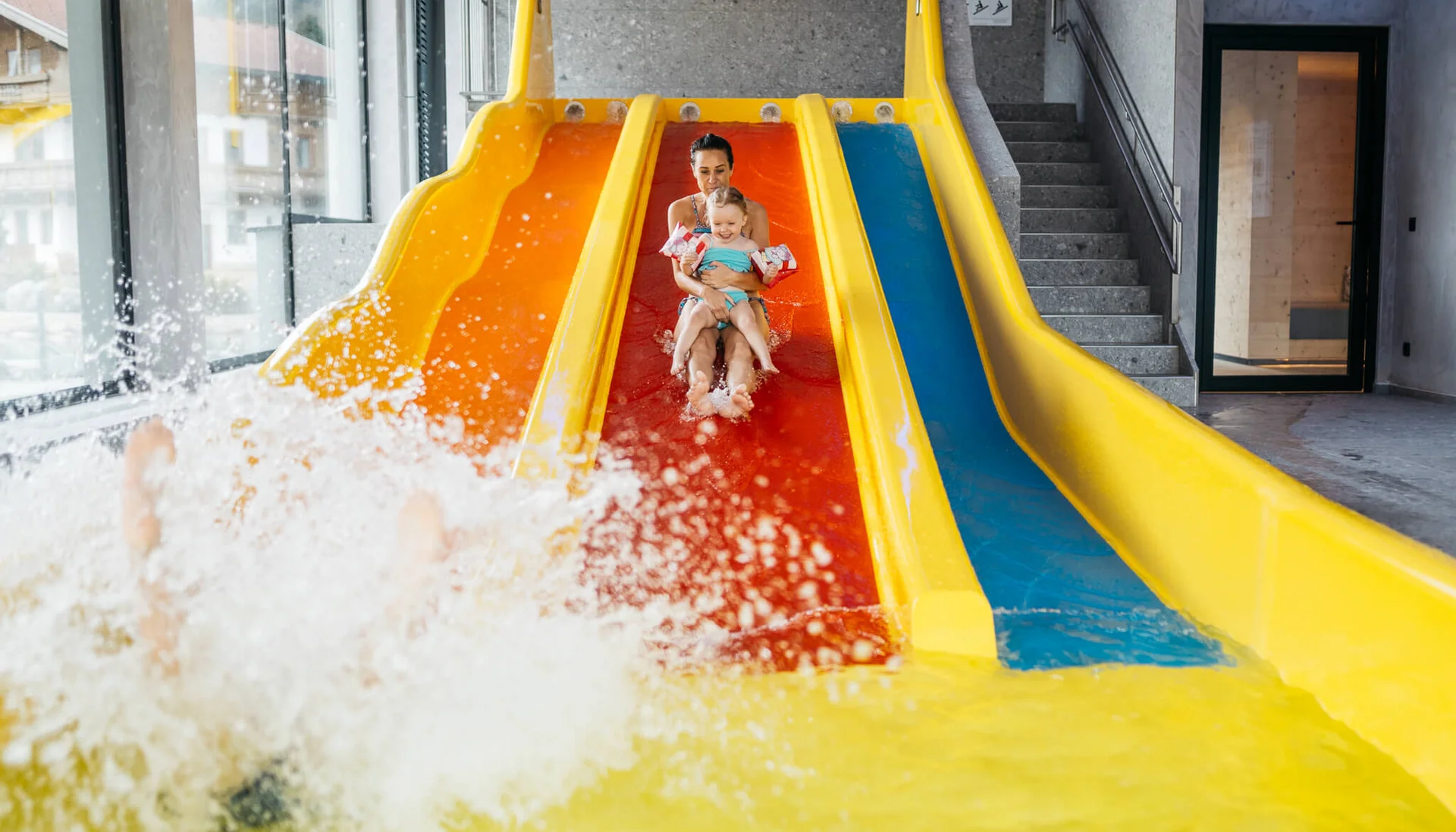 Ihr Hotel für Alleinerziehende Frau und Kind rutschen zusammen eine gelb-orange Wasserrutsche hinunter im Schwimmbad