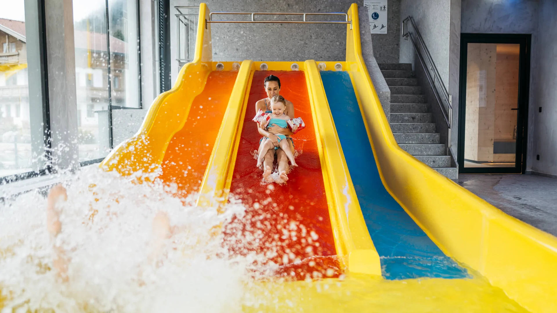 Ihr Familienhotel in Österreich mit All-inclusive-Angebot Frau und Kind rutschen zusammen eine gelb-orange Wasserrutsche hinunter im Schwimmbad