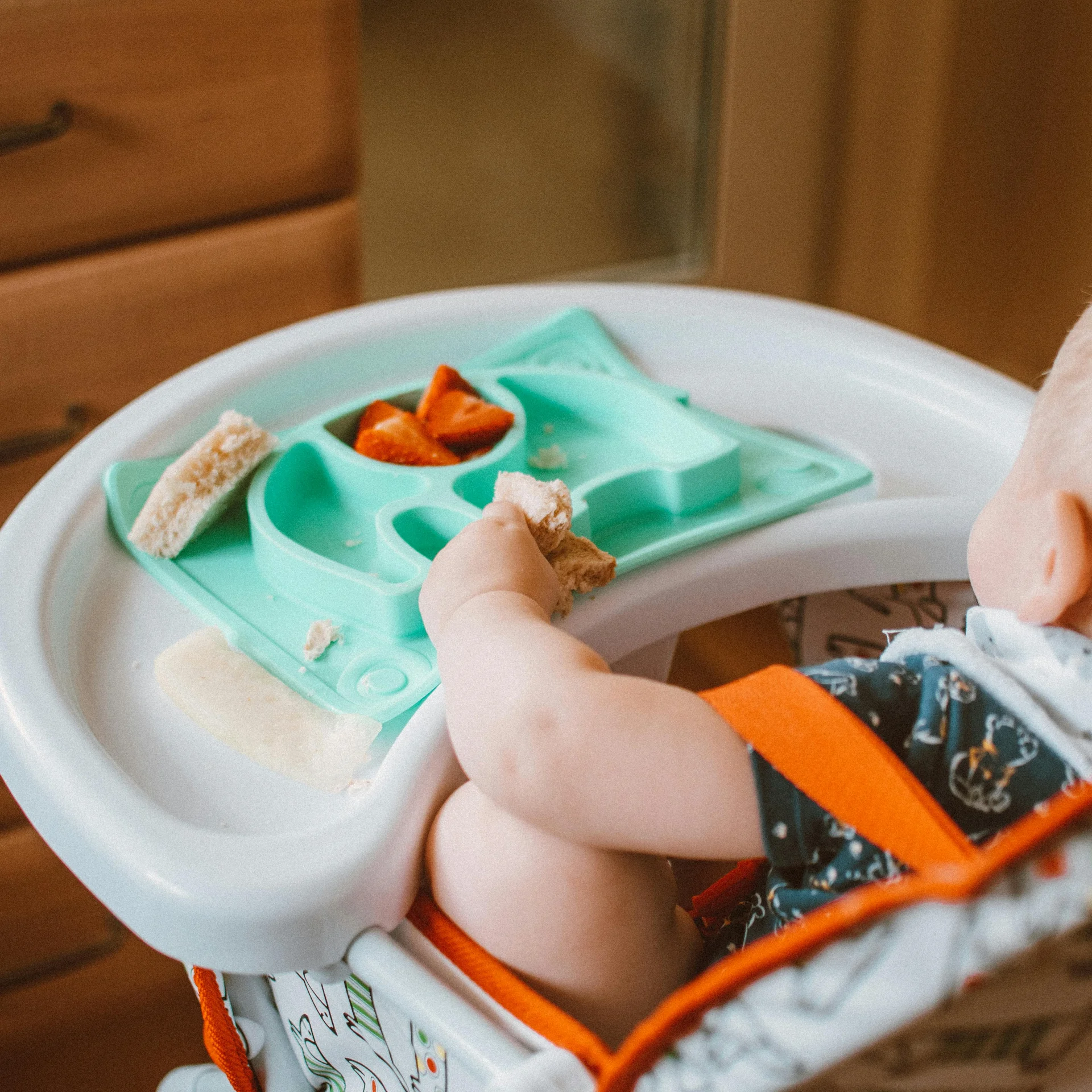 Familienurlaub mit Baby und Kleinkind im Buchau Baby im Hochstuhl isst Brot und Erdbeeren von einem blauen Teller